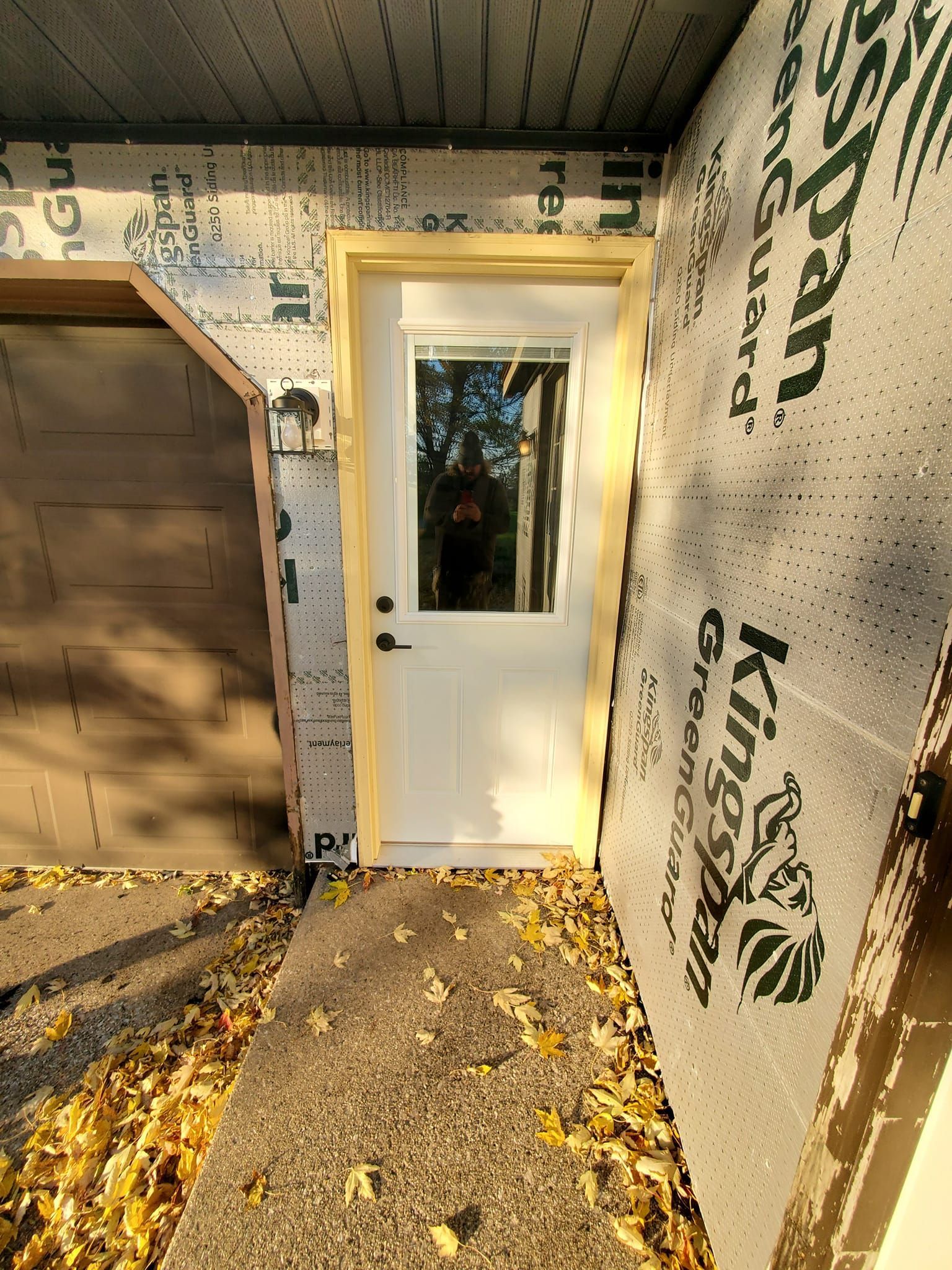 Front porch with white door and tan siding, sunlight casting shadows on the floor.