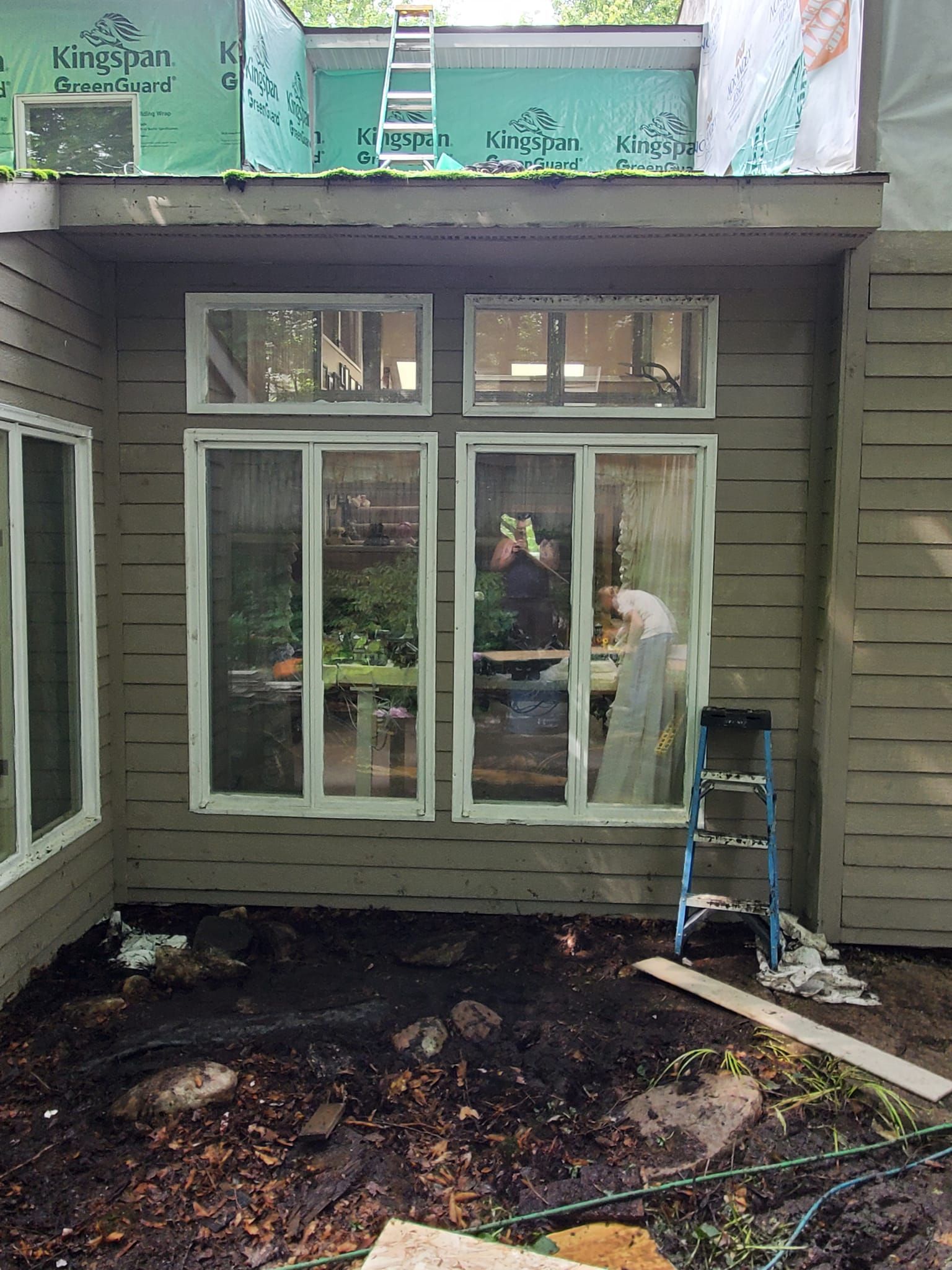Porch under construction with white French doors, exposed dirt, and a ladder beside the entry.