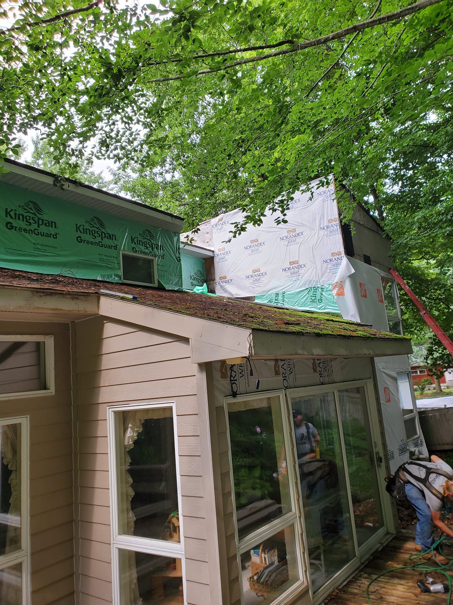 Small storefront under leafy trees, with a green awning, glass door, and a person near the entrance.