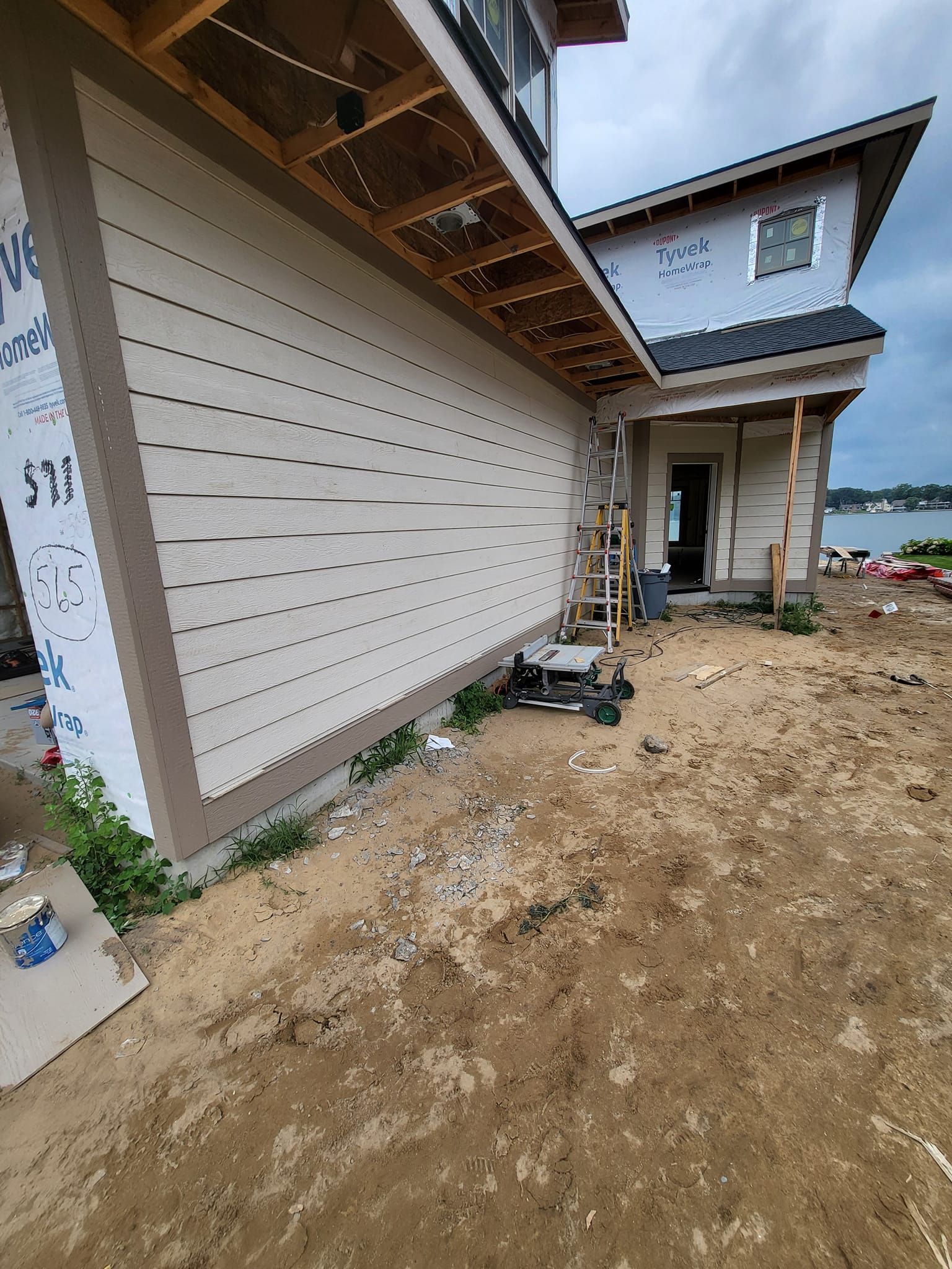 New house exterior with white siding, exposed roof overhang, and muddy construction site foreground