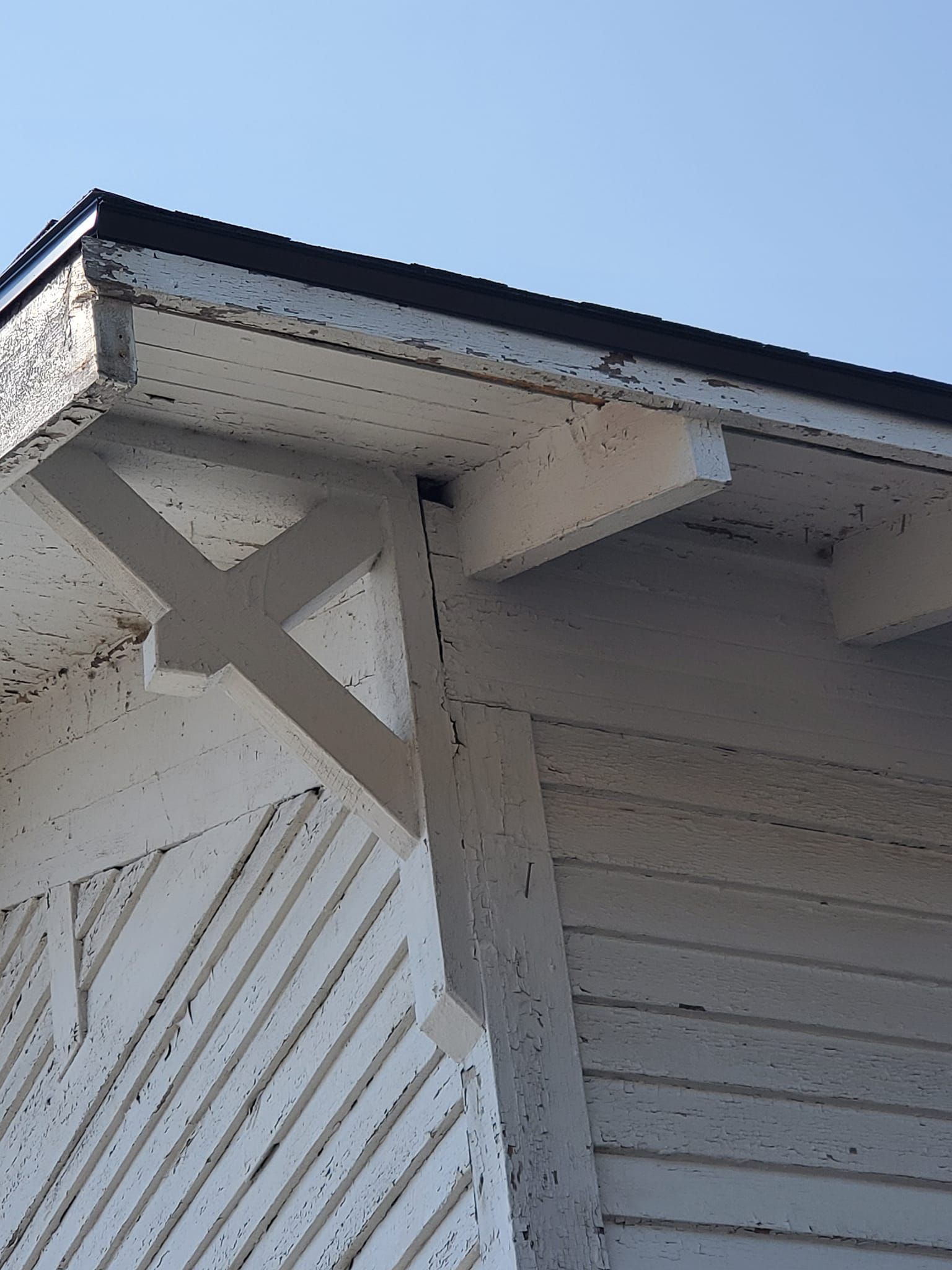 White house exterior corner with blue trim and decorative support beams under the roofline
