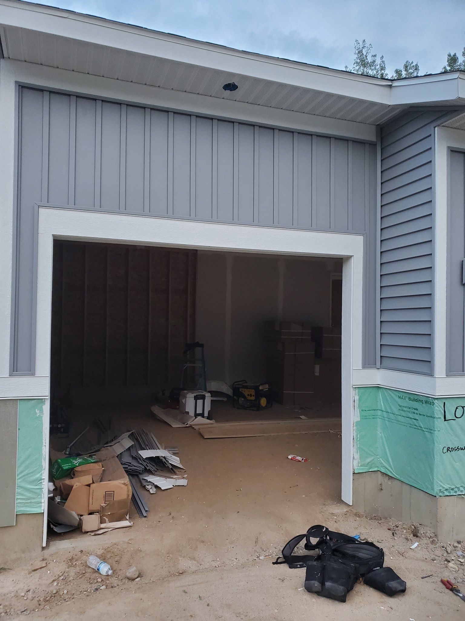 Partially open garage with construction debris and boxes on the floor, gray siding and white trim.