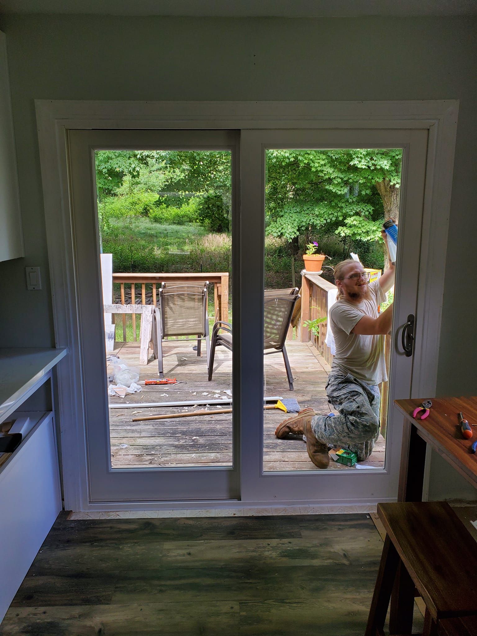 Worker on a deck beside an open sliding door, carrying a white object near a home interior.