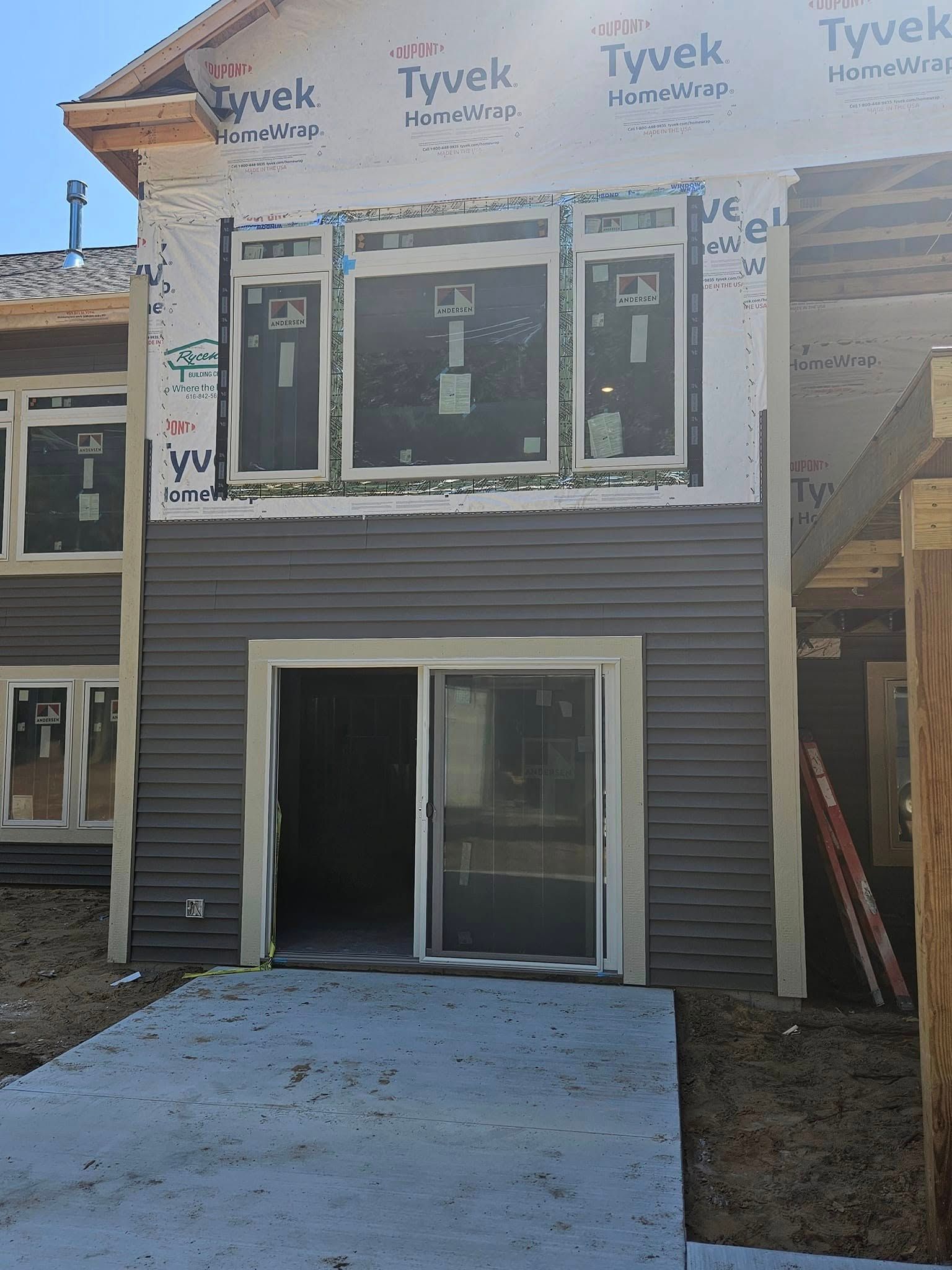 Partially built two-story house with gray siding, large windows, and a front concrete walkway under construction.