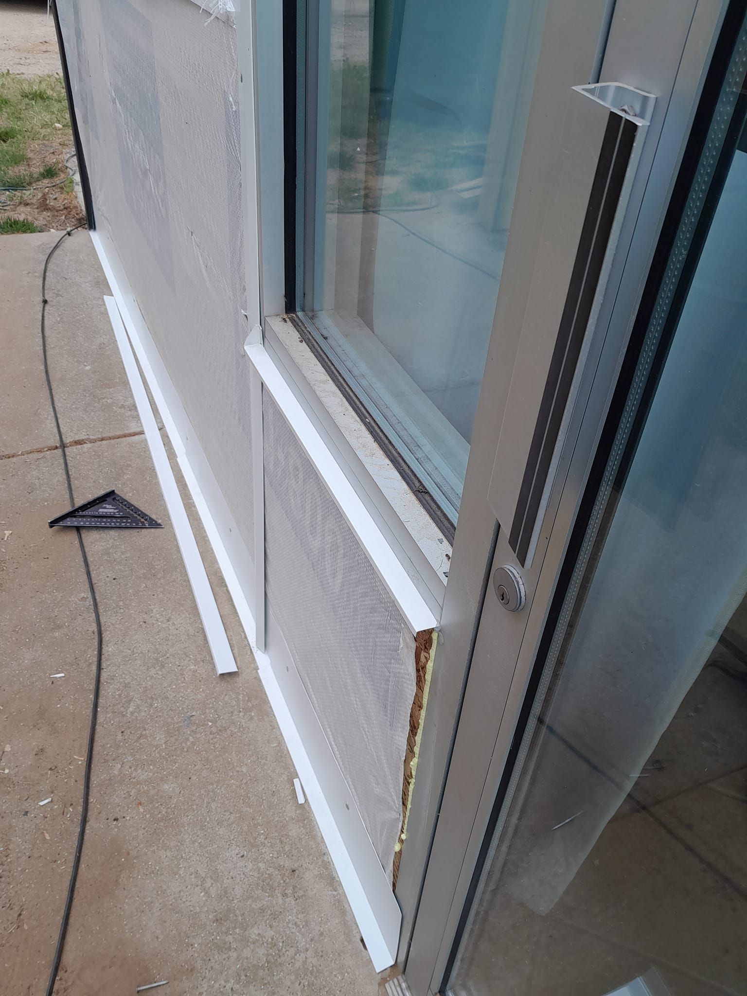 White trim board leaning against an exterior sliding glass door on a patio, with a small black triangular tool nearby