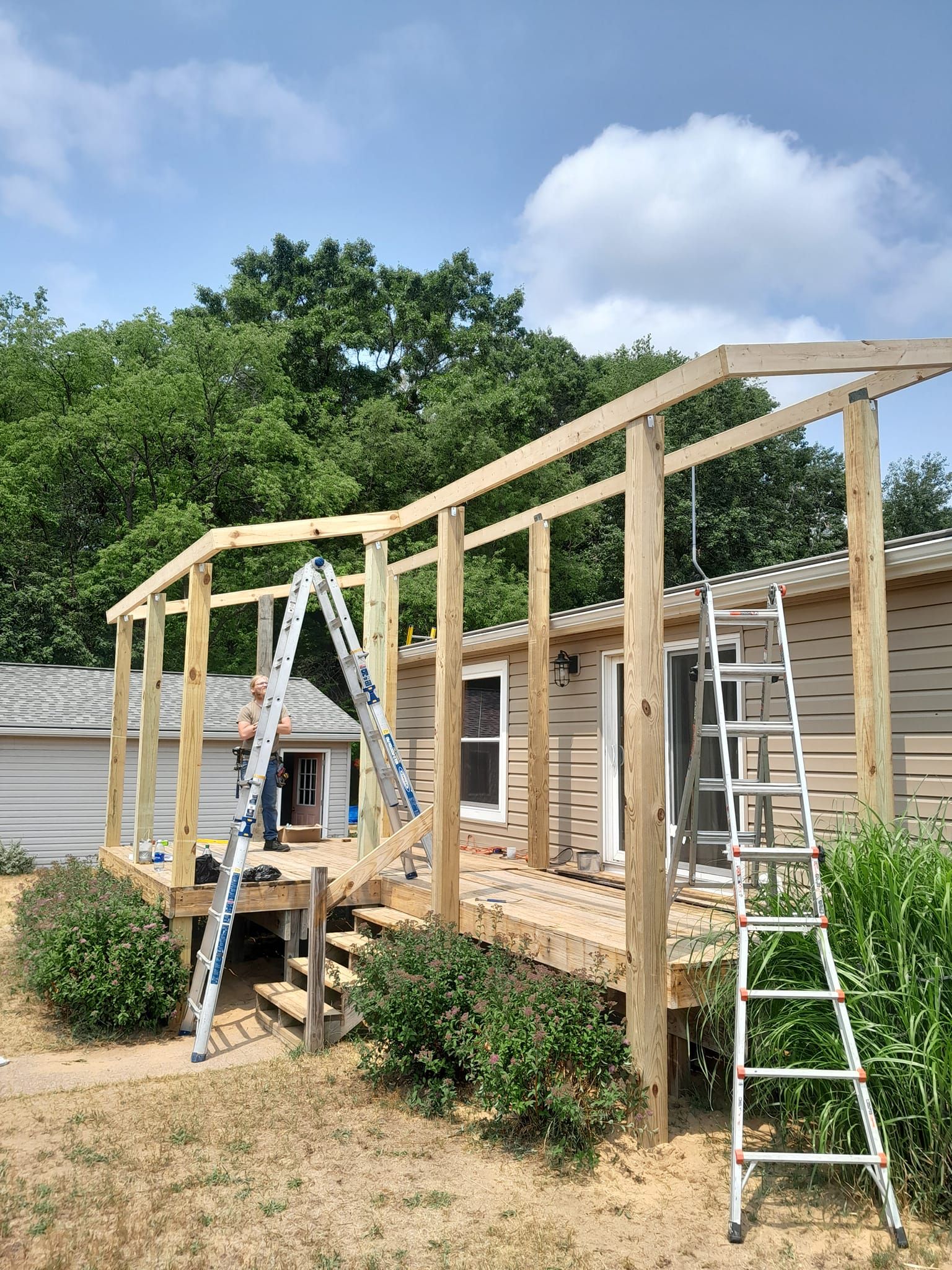 House under construction with wooden framing, ladders, and a partially built porch in a yard