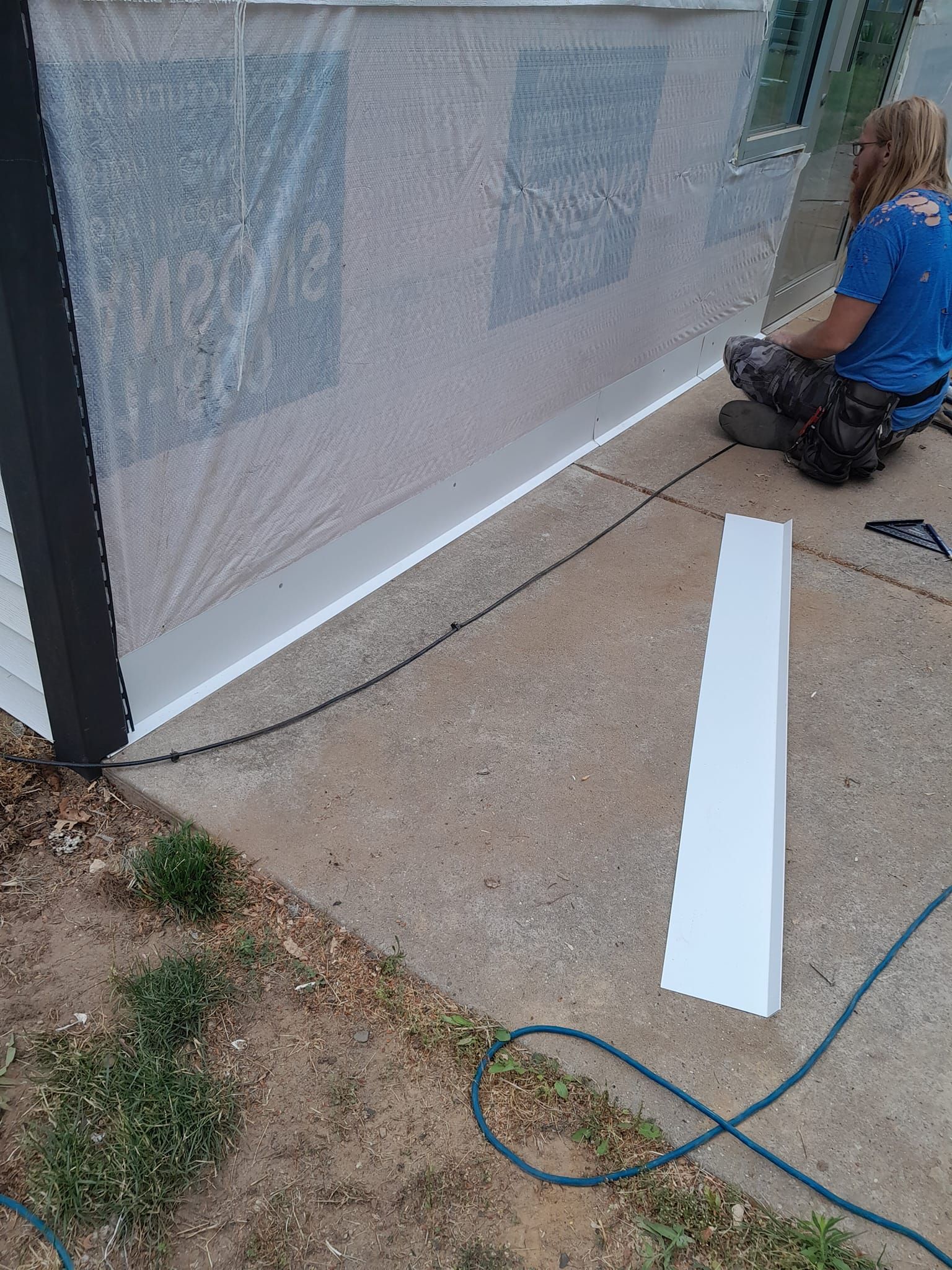 Person working on a white barrier beside a patio, with a hose on the ground.