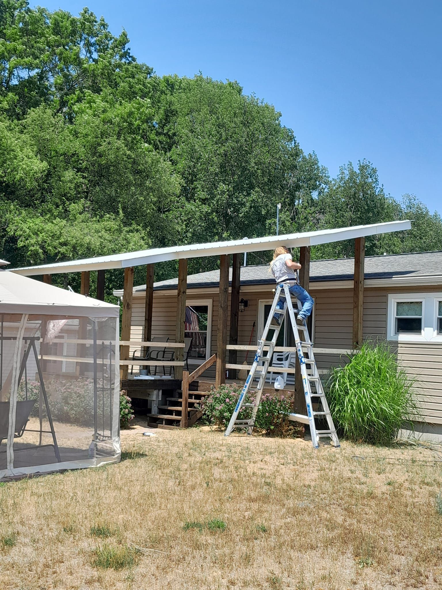 Person on ladder installing solar panels on a small house roof in a sunny yard