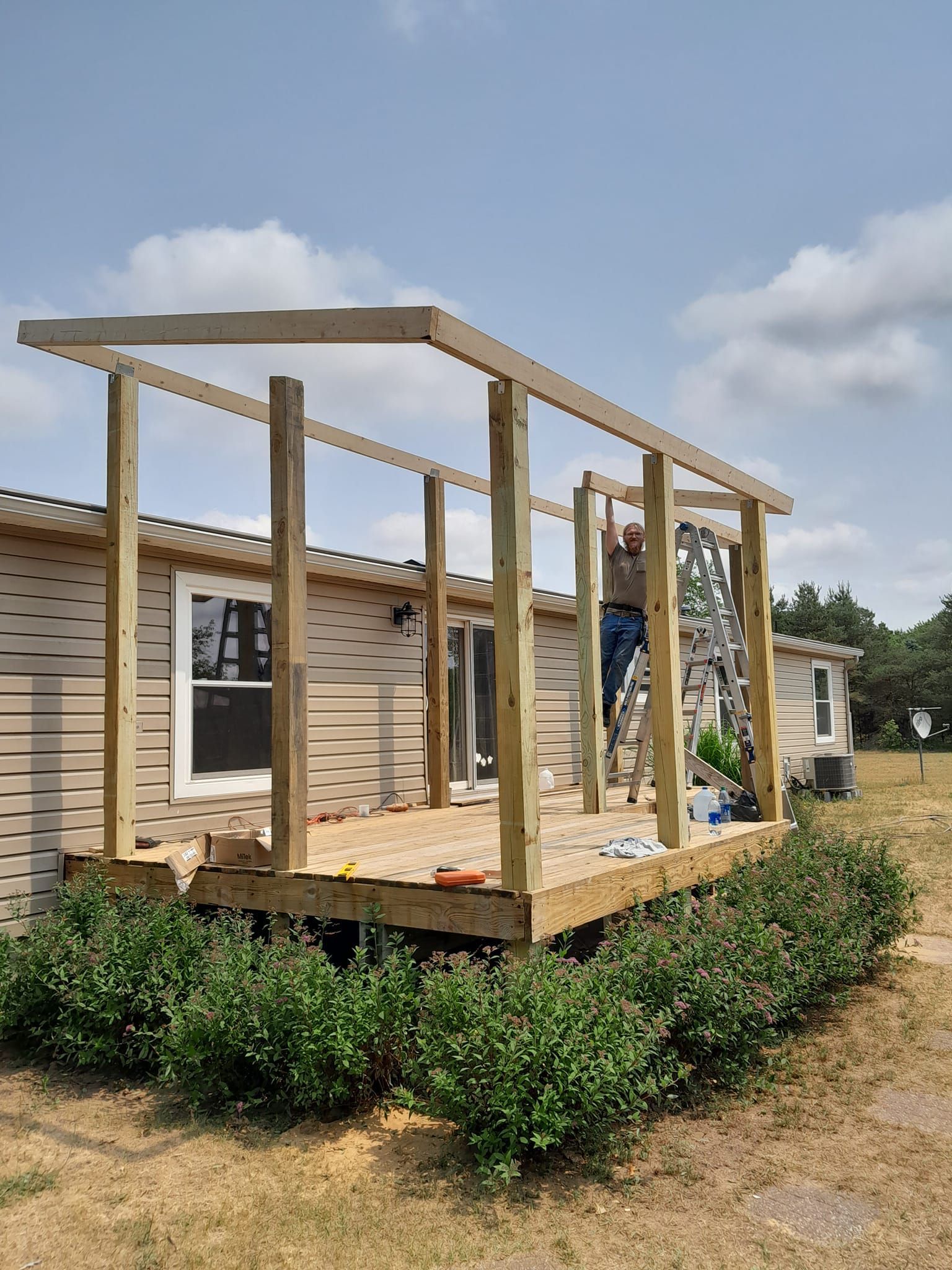 Partially built wooden porch frame on a house with posts and roof beams under a blue sky
