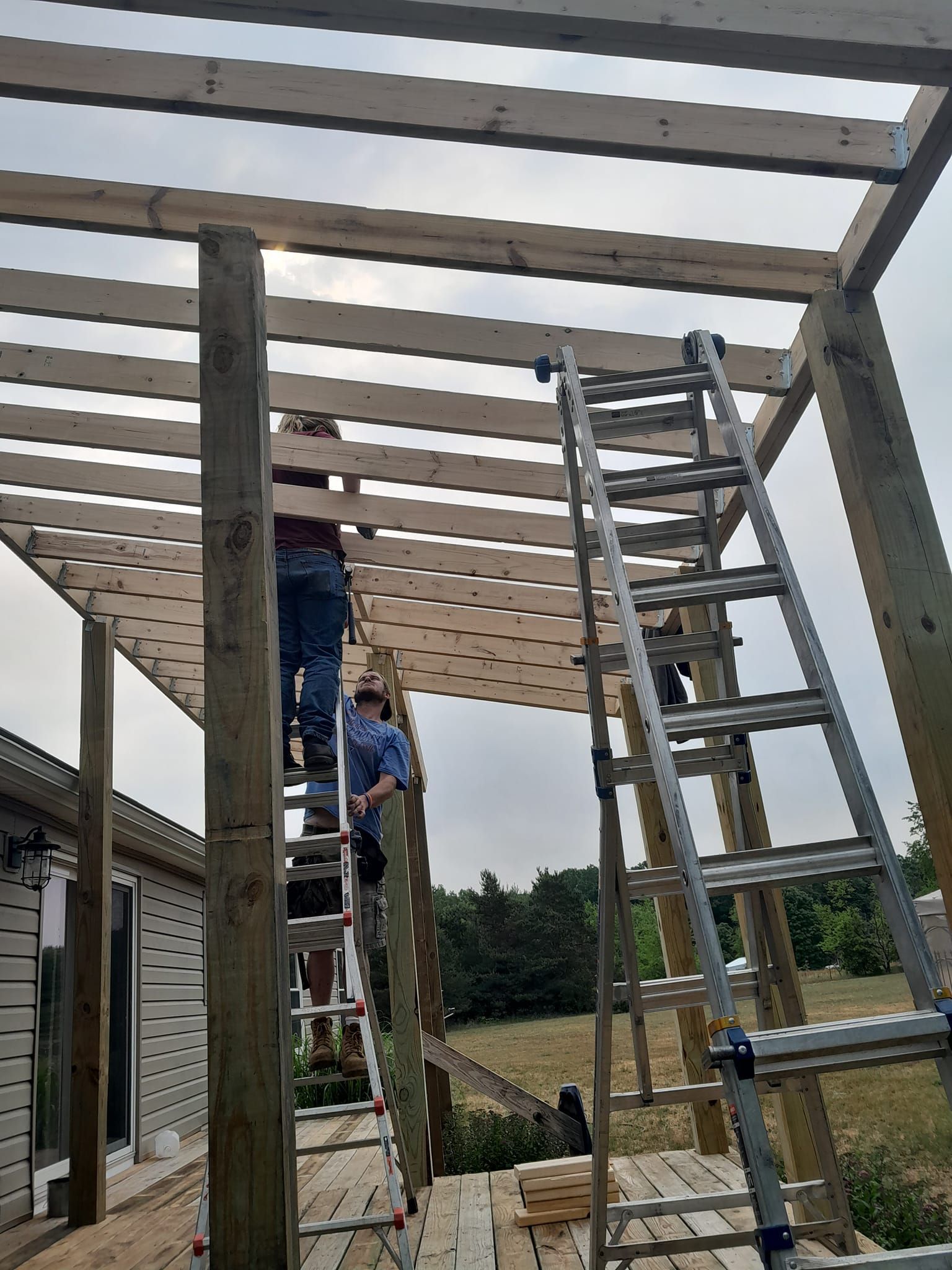 Workers on ladders building a wooden pergola frame outdoors