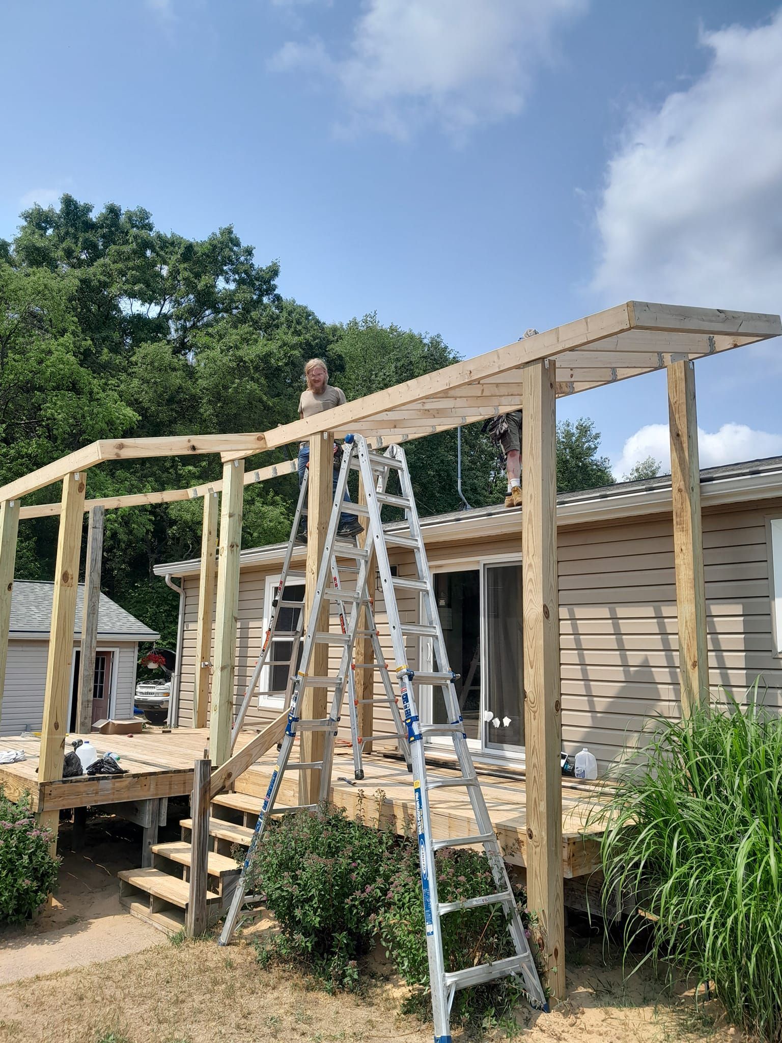 Two ladders at a house under construction with unfinished wooden framing and roof beams under a blue sky