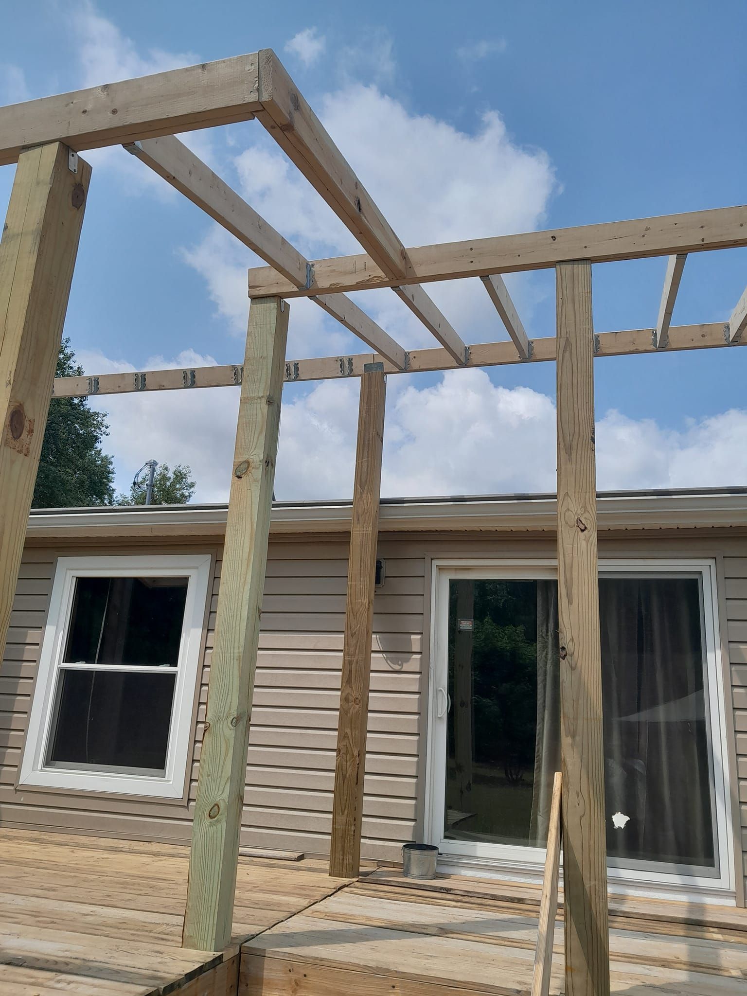 Partially built wooden deck frame attached to a house under a blue sky