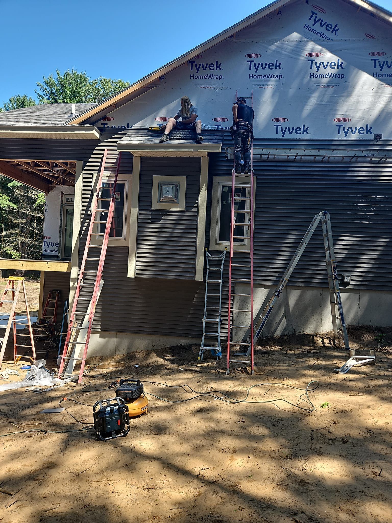 Two ladders against a house under construction with workers on the roof and siding exposed.