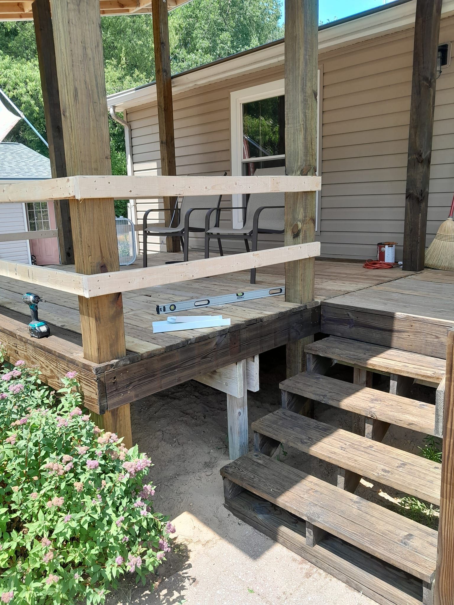 Wooden porch stairs and railings leading to a tan house exterior with a patio area.