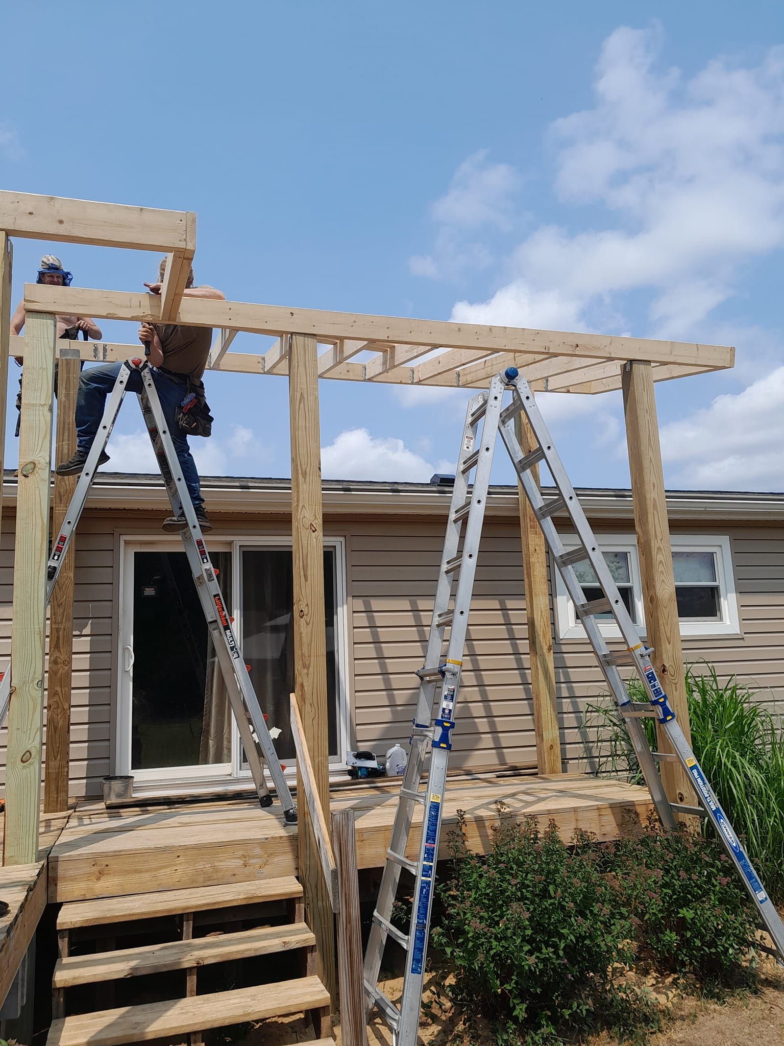 House porch under construction with wooden framing, ladders, and blue sky above