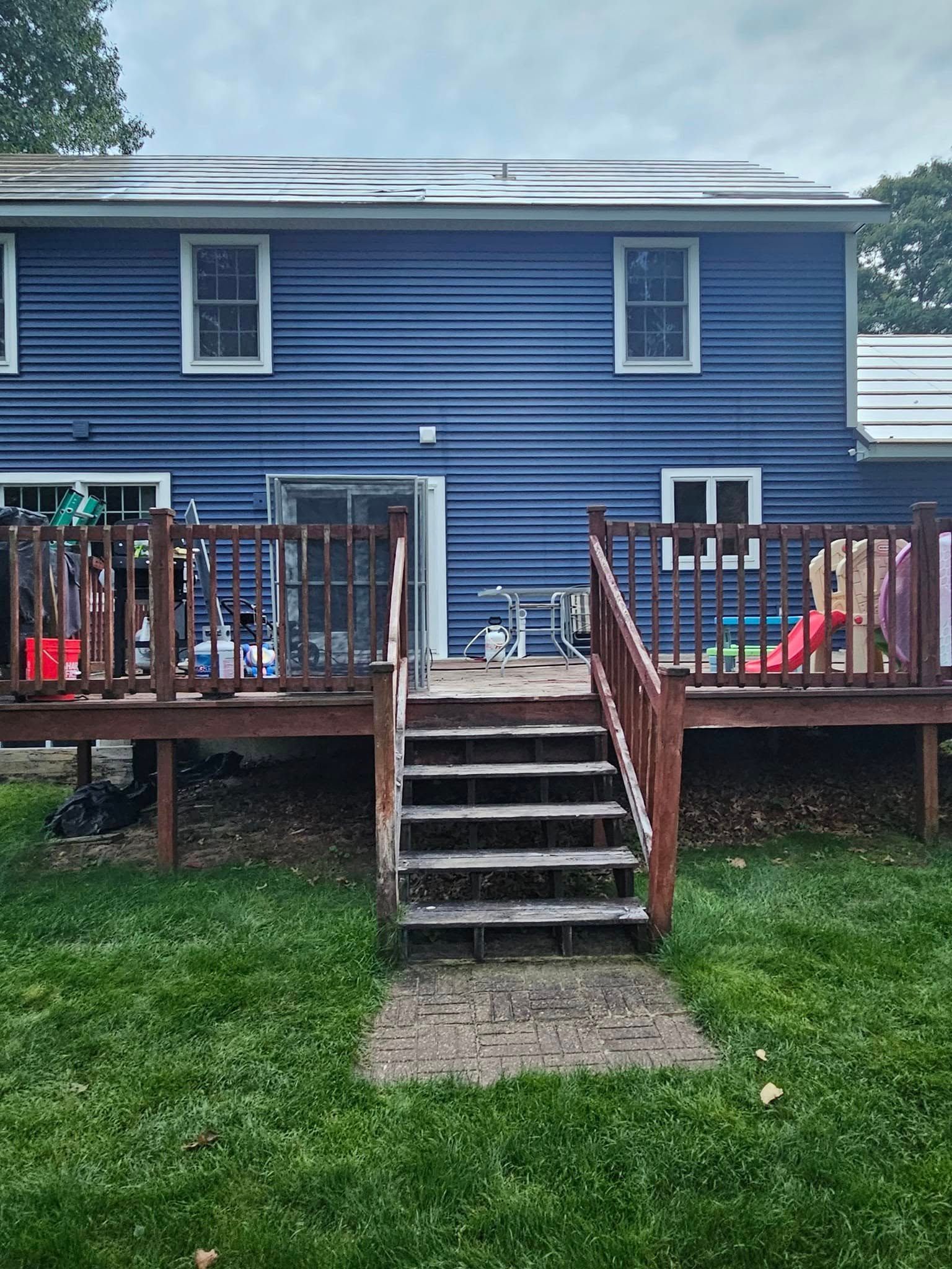 Blue house exterior with wooden deck, stairs, and chairs leading to a grassy yard