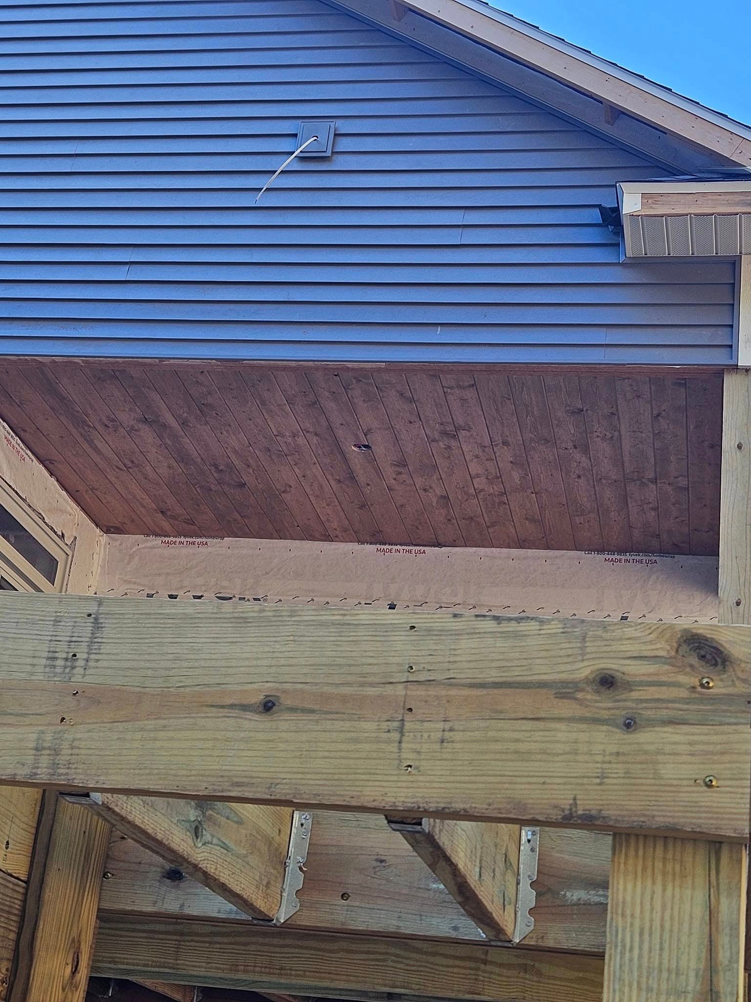 Partially built wooden structure with blue siding and exposed framing against a house wall