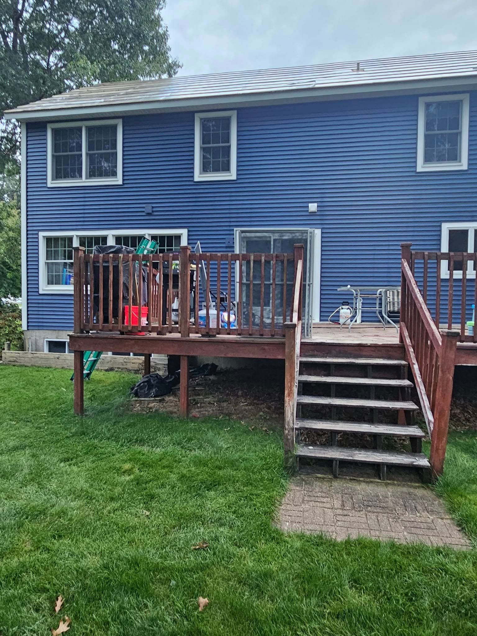 Blue two-story house with a raised wooden deck, stairs, and grassy yard