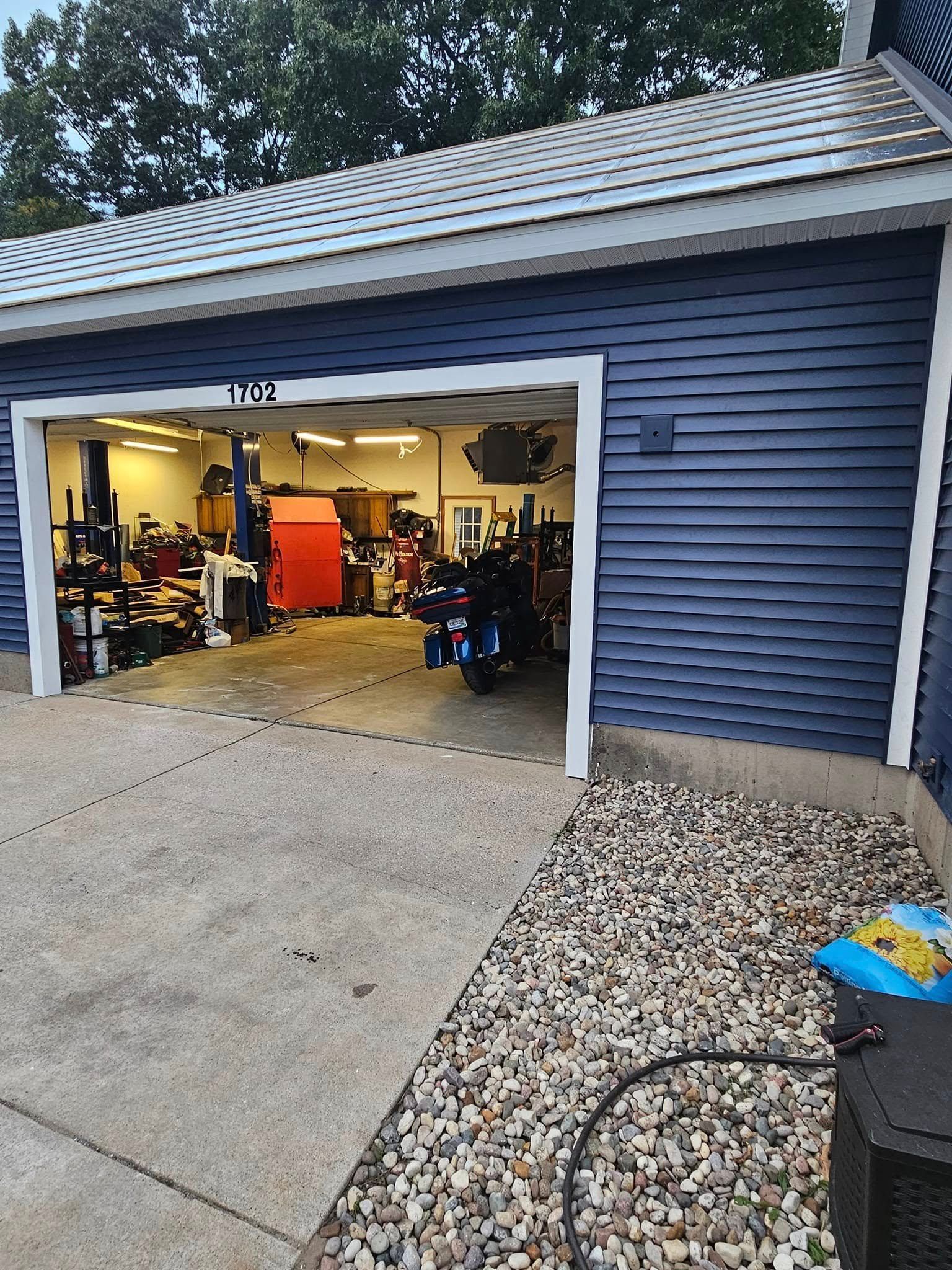 Open garage with blue siding, a red cabinet, and bicycles inside, viewed from a driveway