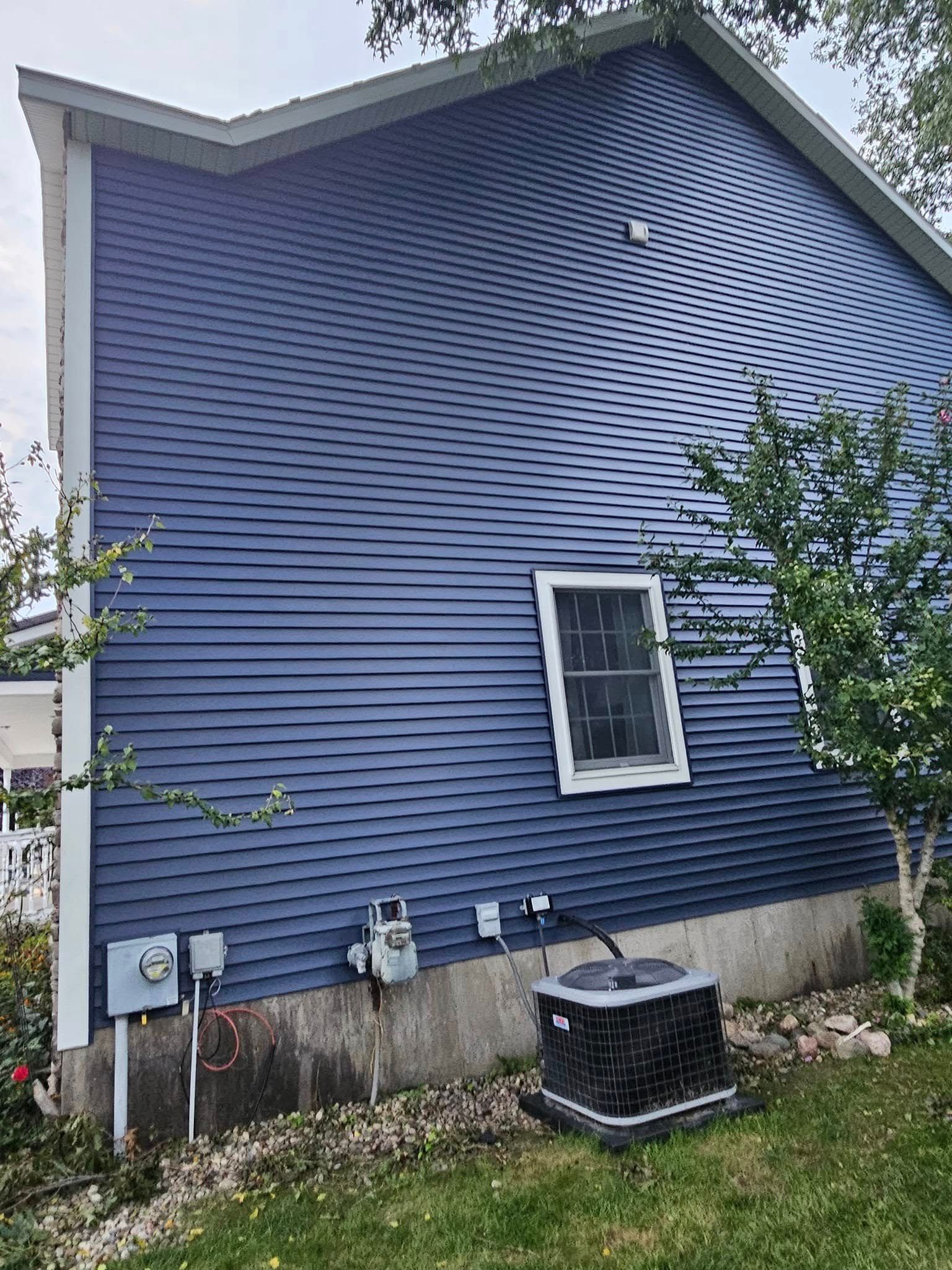 Blue vinyl-sided house exterior with a small window, utility meters, and an air conditioner unit.