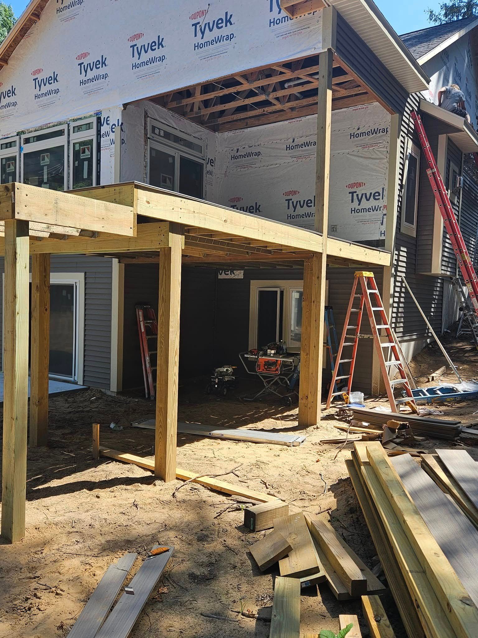 Partially built house addition with exposed framing, ladders, and construction materials in the yard