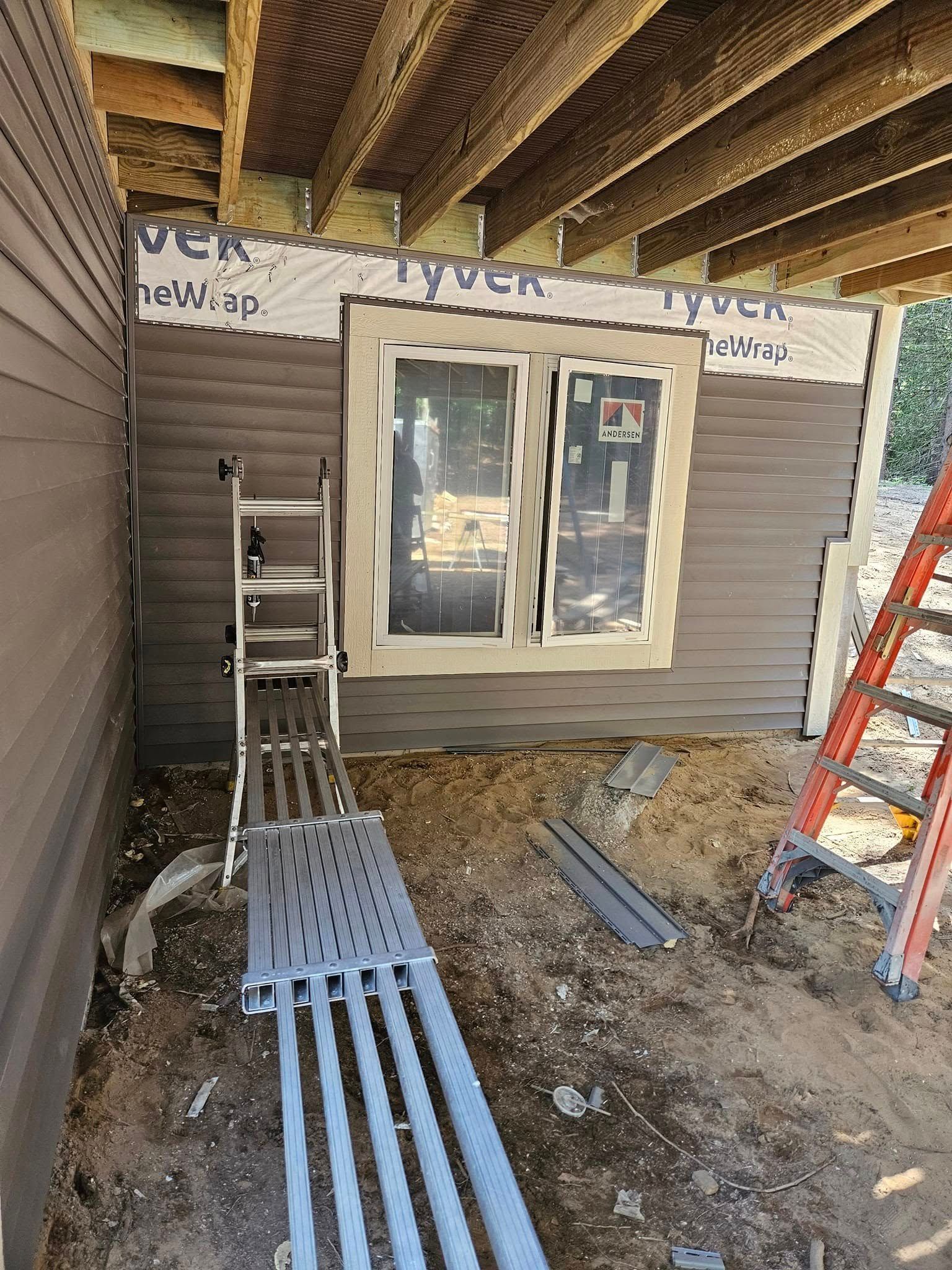 Construction area with window, ladder, and scaffold planks outside a house under renovation