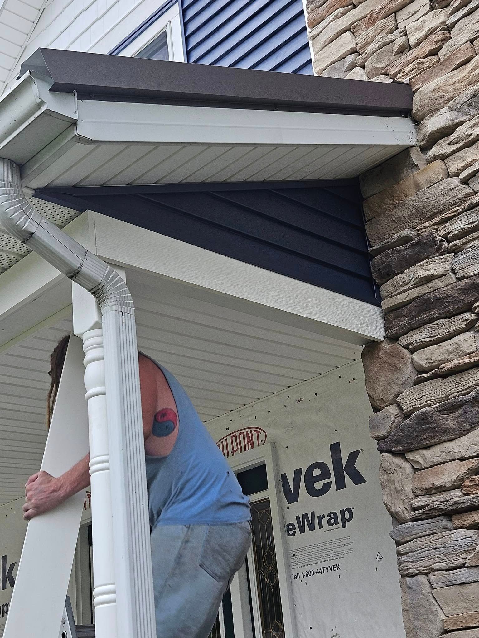Worker installing a white porch awning beside stone siding and dark blue trim