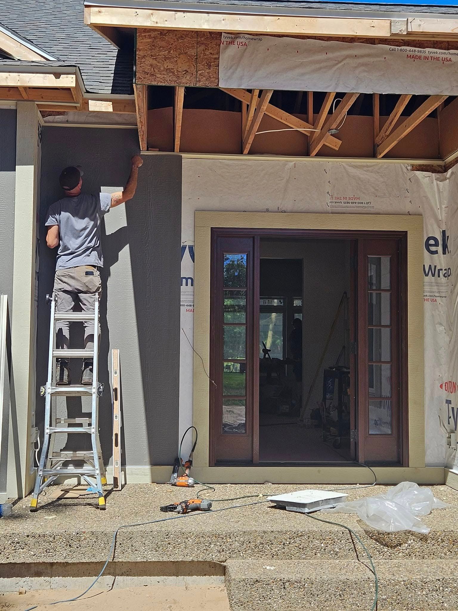 Worker on ladder installing trim under a roof overhang at a house entrance under construction
