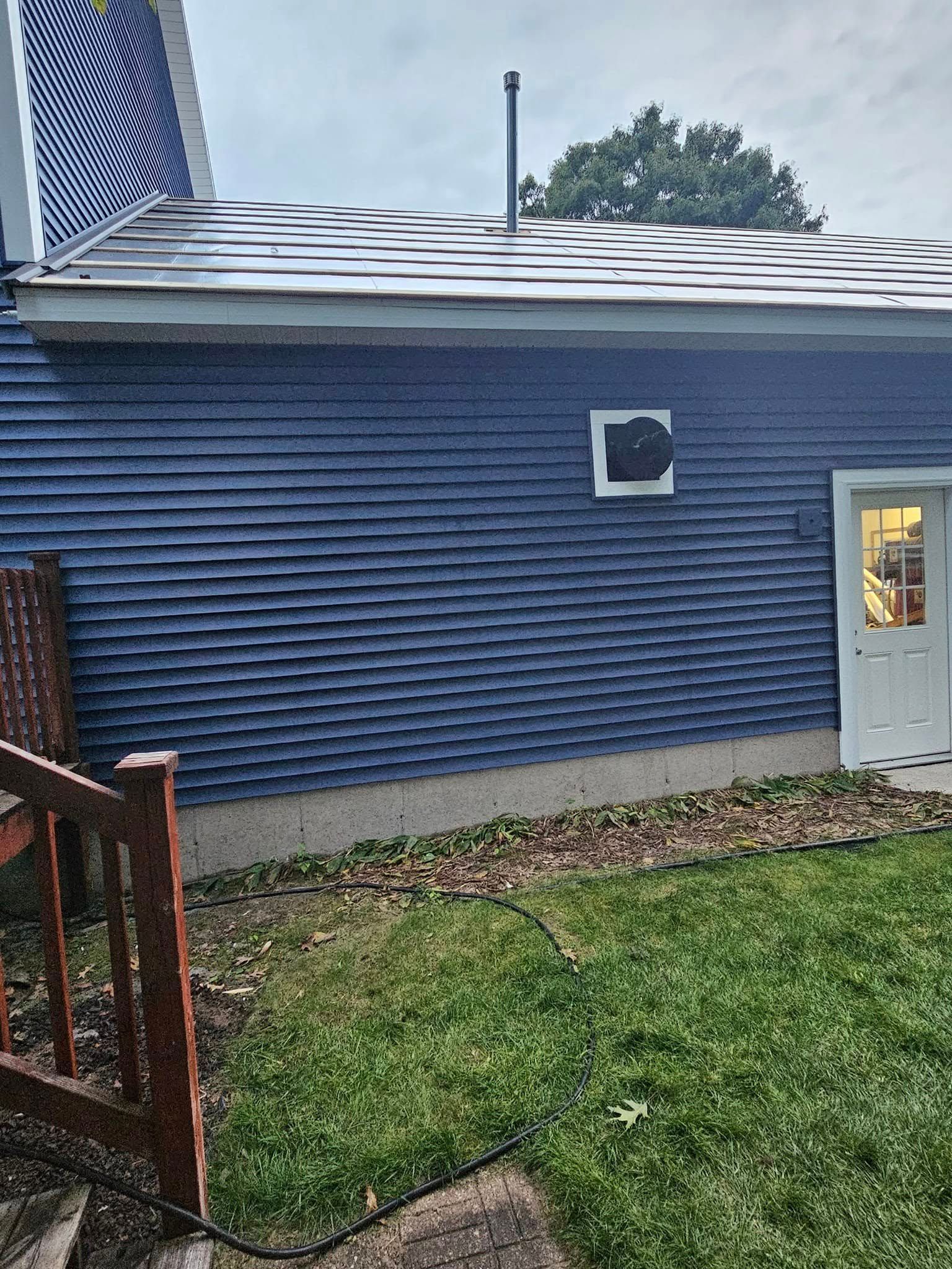 Blue-sided house exterior with a small window, white door, and grassy yard
