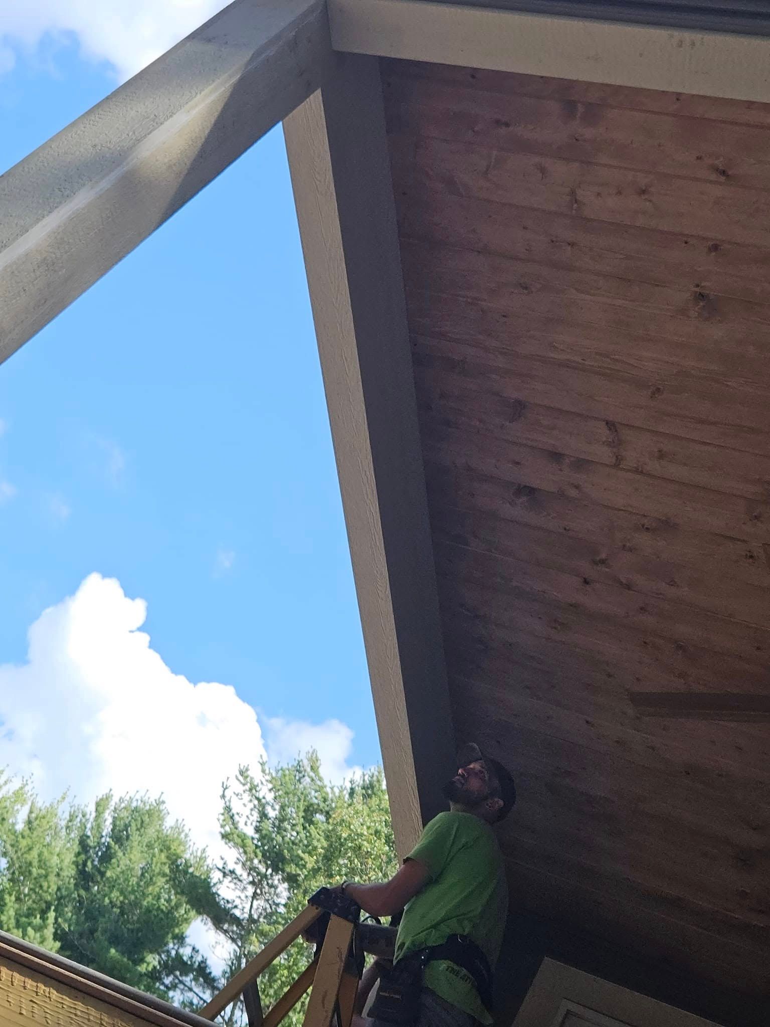 Person on a ladder under a wooden roof, reaching up against a blue sky.