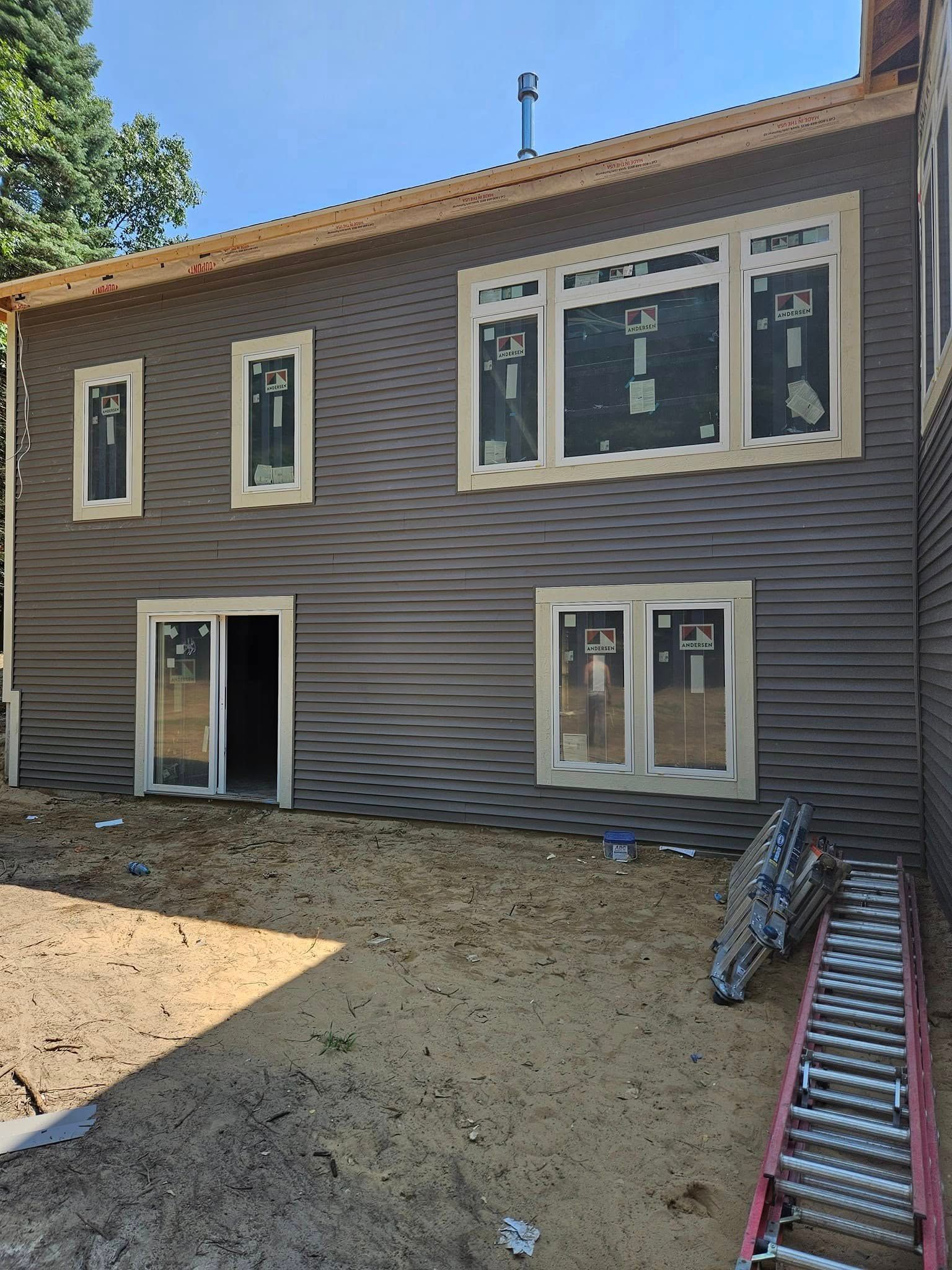 Two-story house under construction with unfinished siding, new windows, and a dirt yard.