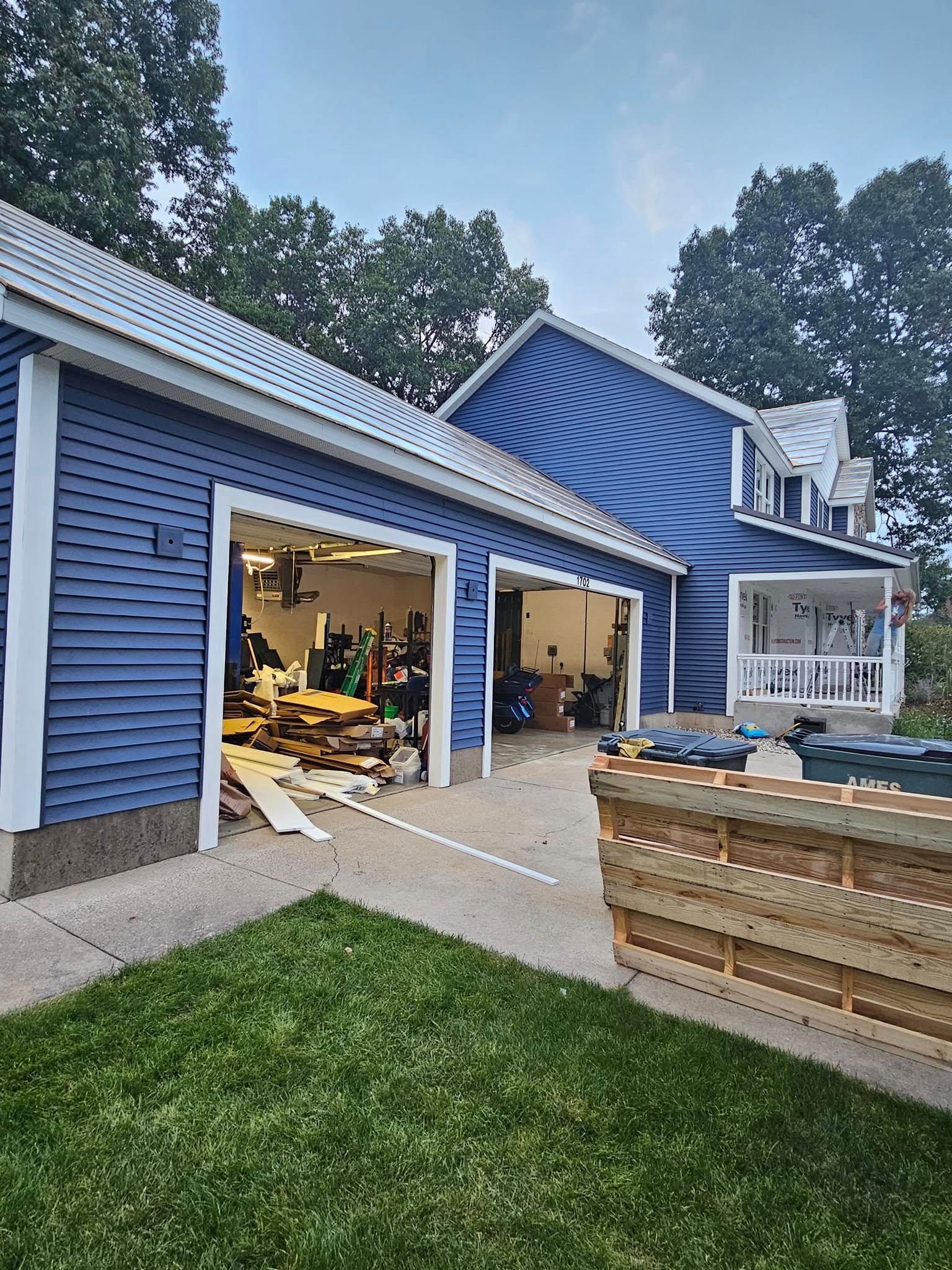 Blue house with open garage after storm damage, debris on driveway, and a damaged fence in front.
