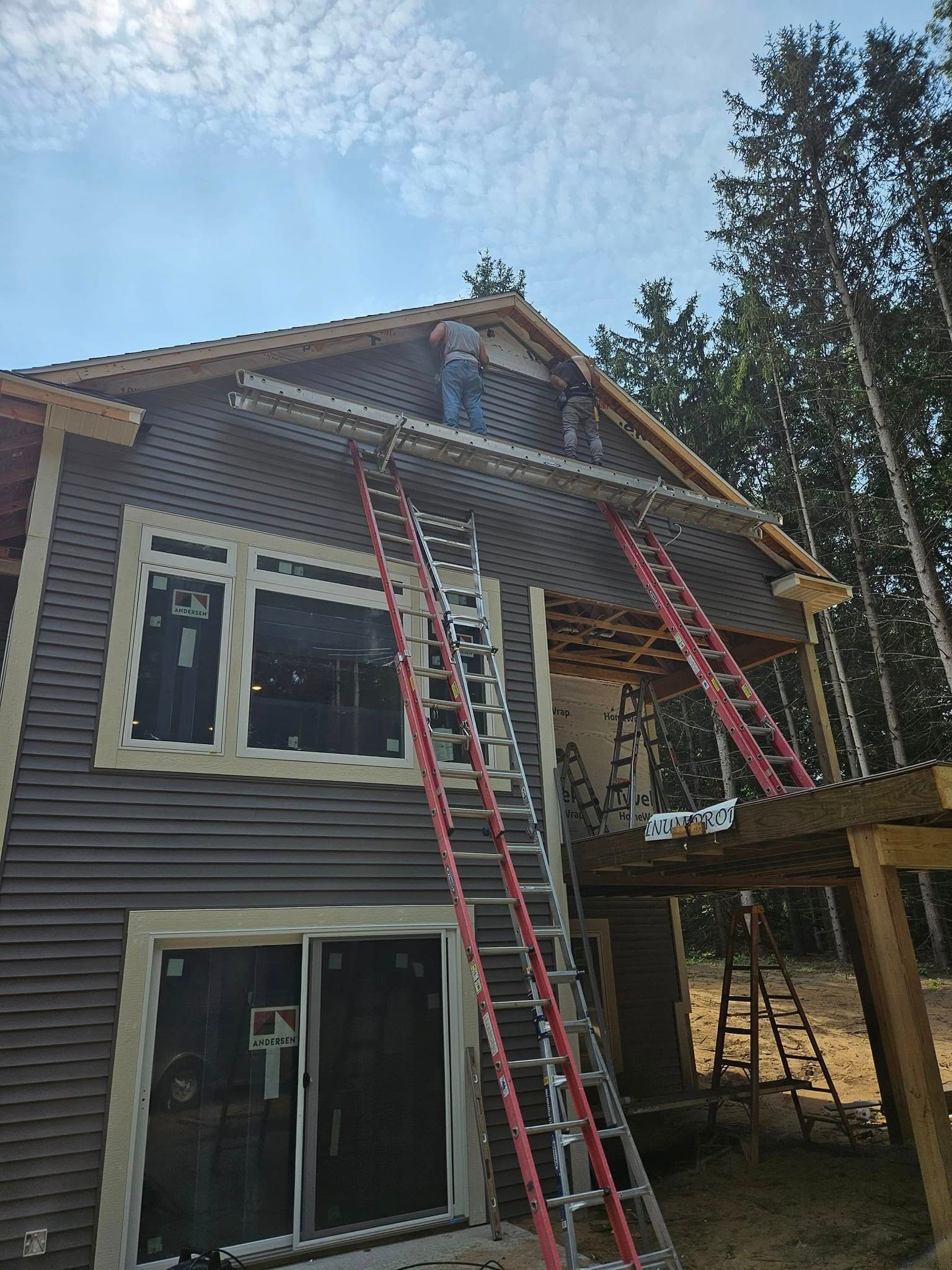 Two extension ladders leaning against a house under construction with roof scaffolding and clear sky