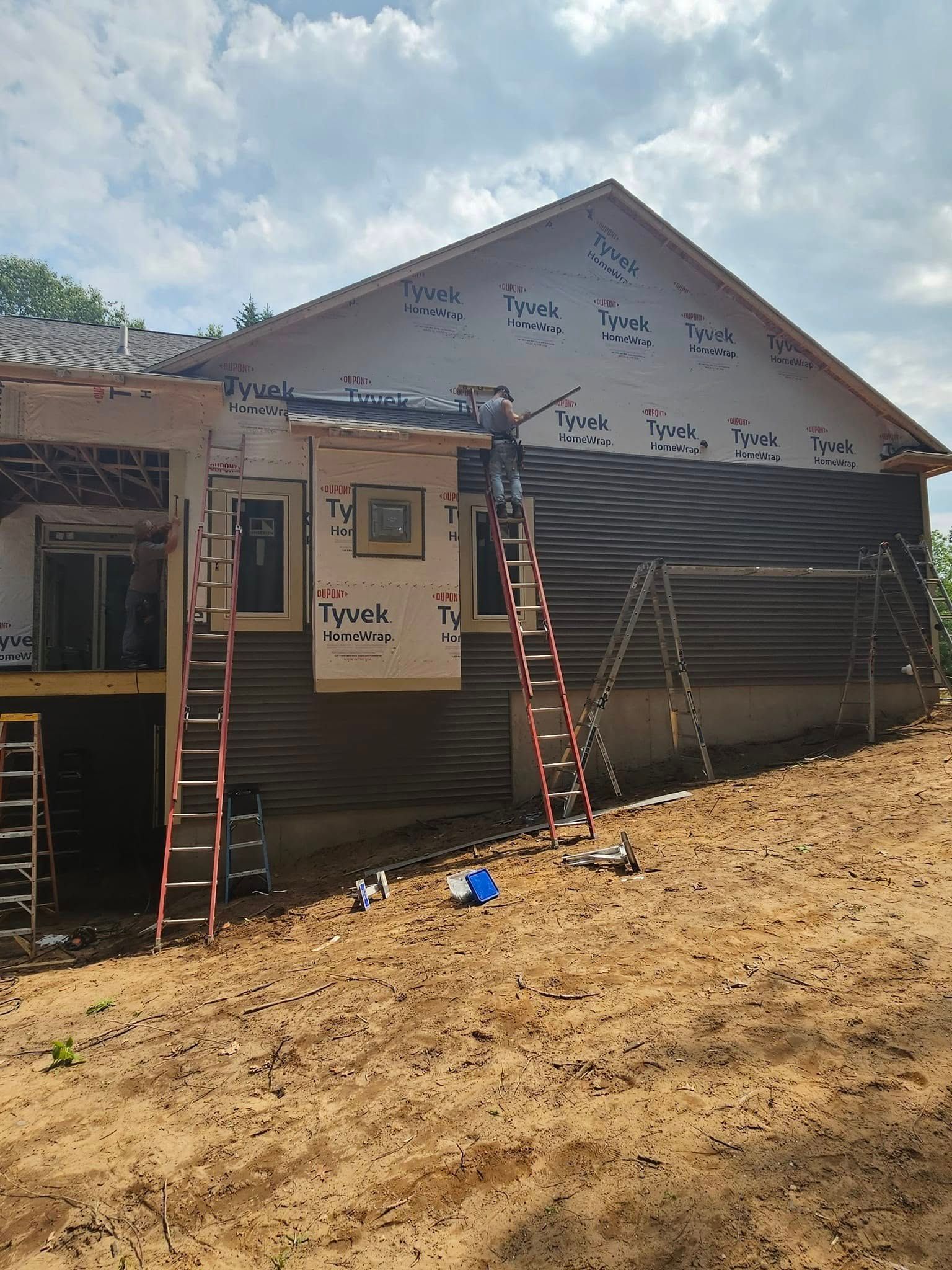 House under construction with two ladders leaning against a white gable wall and dirt foreground