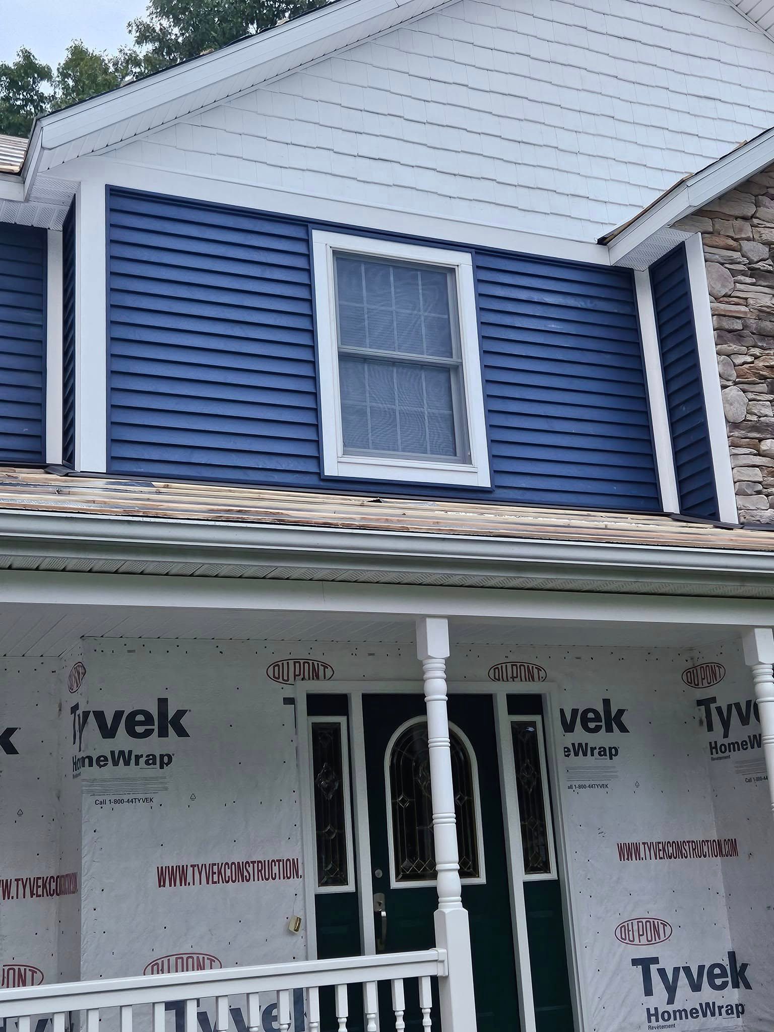 Blue house siding and white trim with a front porch under renovation, showing Tyvek house wrap below.