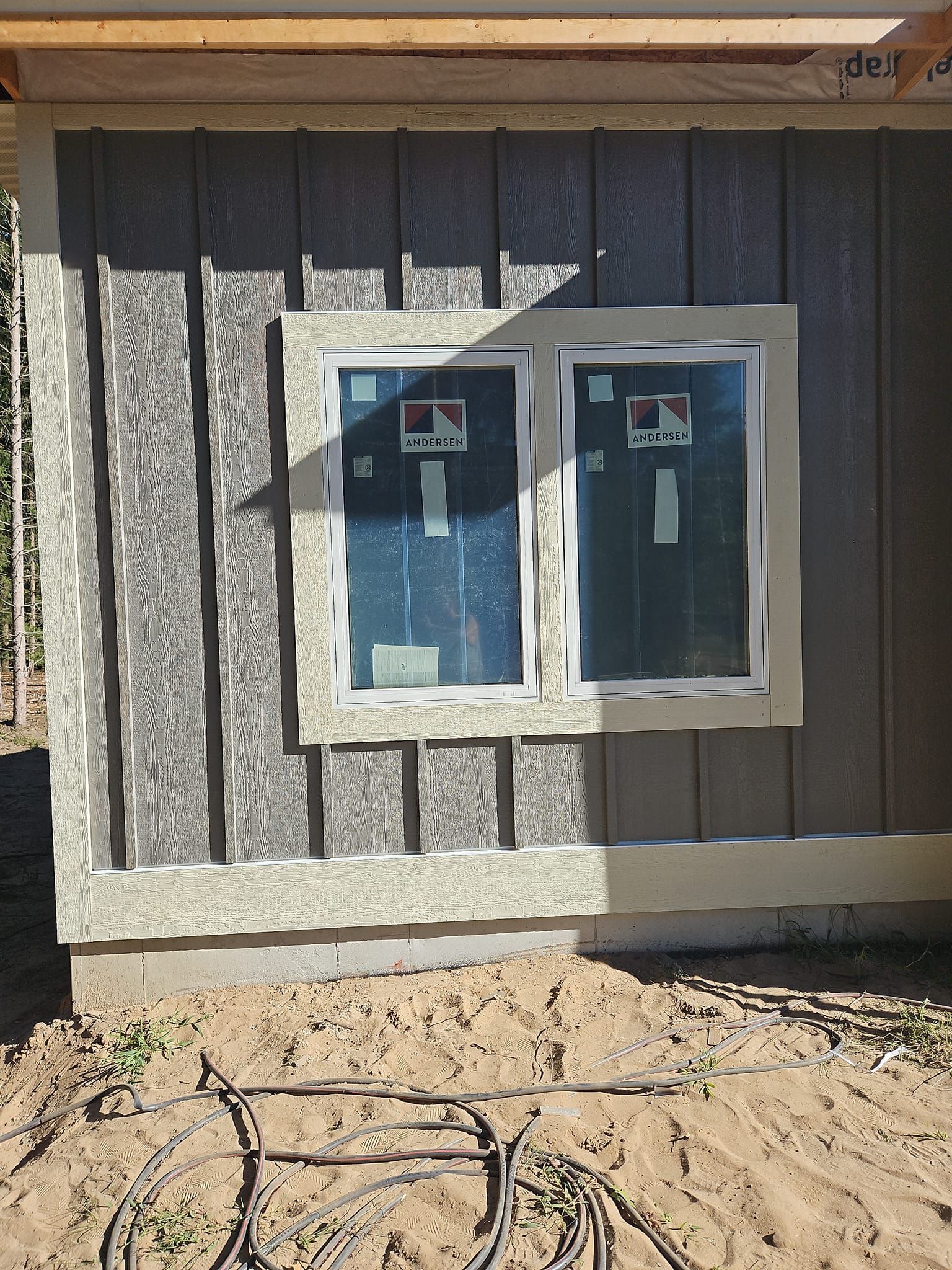 Exterior wall with two windows on a weathered building and sandy ground in front