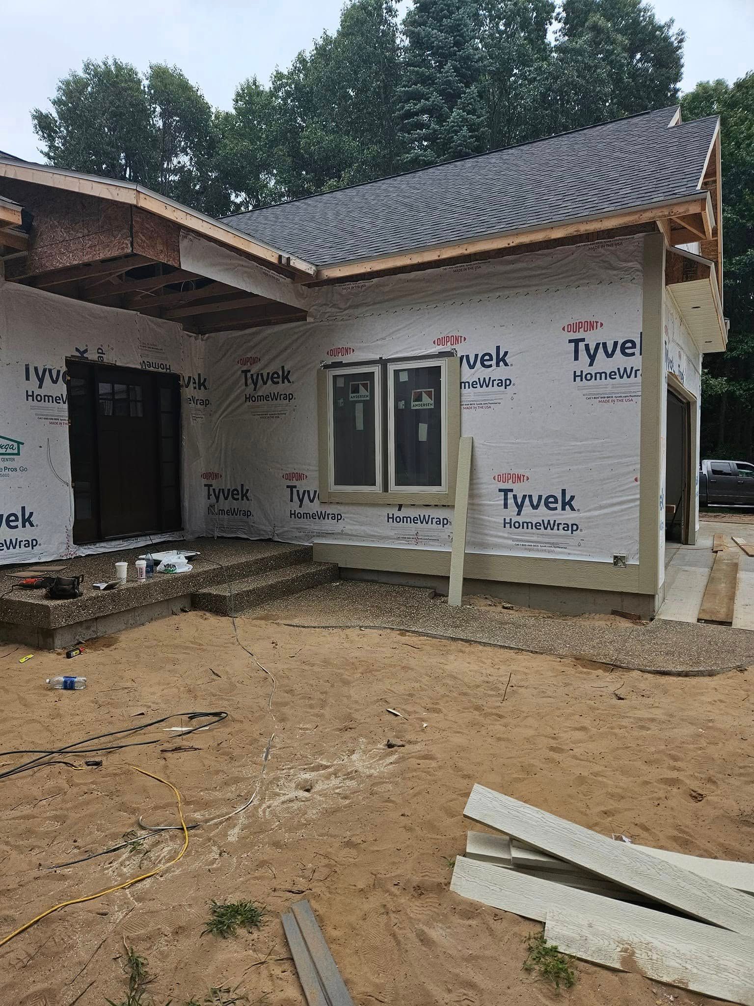 Partially finished house exterior with white walls, dark roof, and dirt yard under construction
