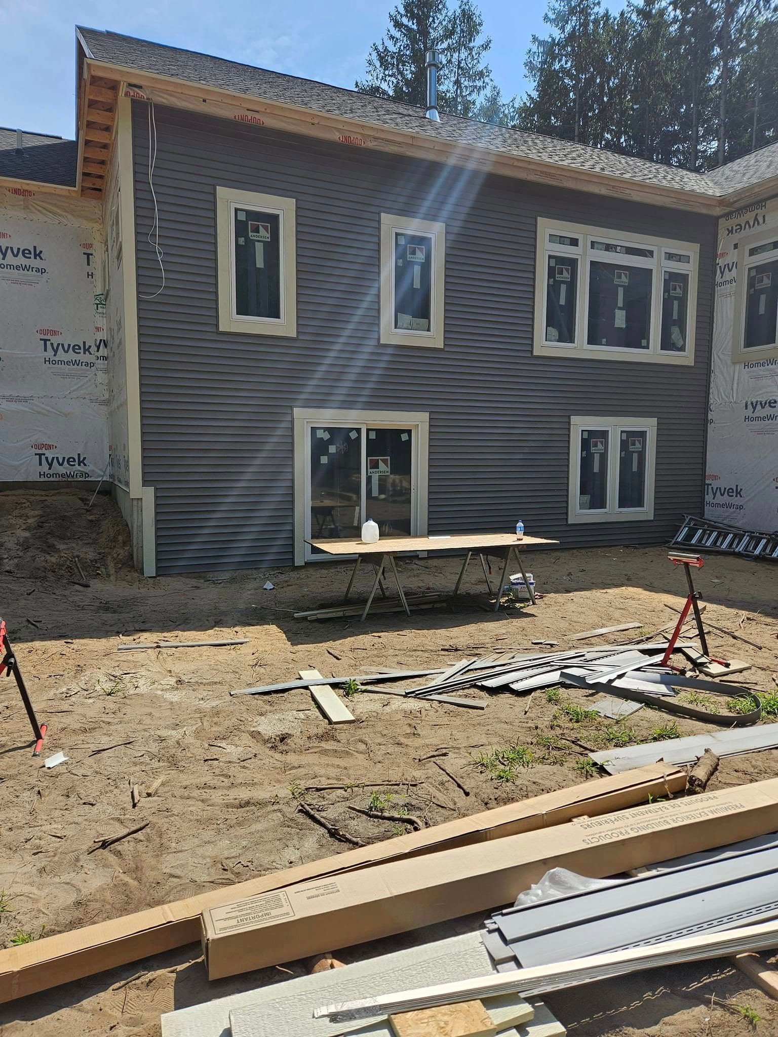 Exterior of a gray house under construction with windows, dirt yard, and building materials in front