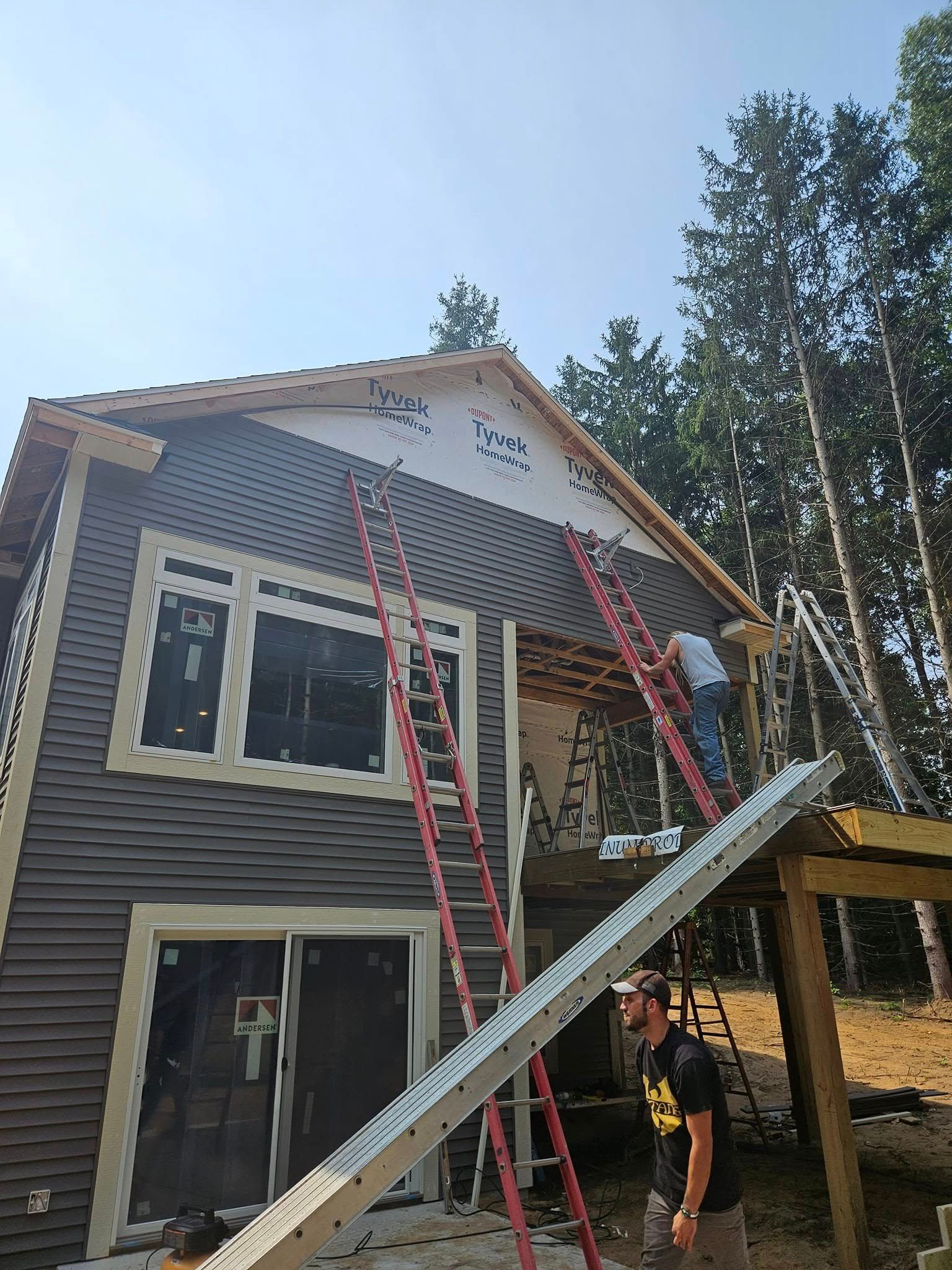 Two-story house with workers on ladders and scaffolding during exterior construction.