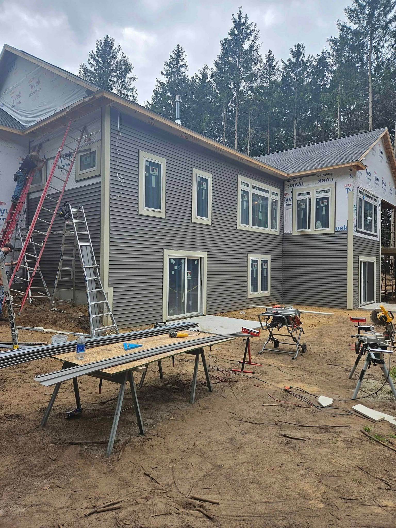 House under construction with siding, ladders, scaffolding, and tools in a muddy yard