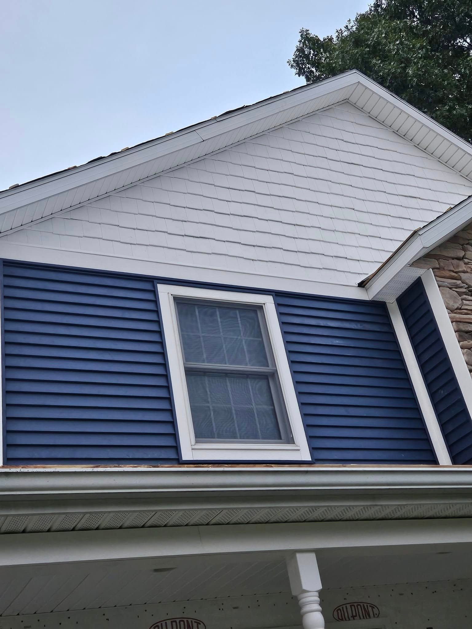 Blue house exterior with white trim, window, and gabled roof under a cloudy sky