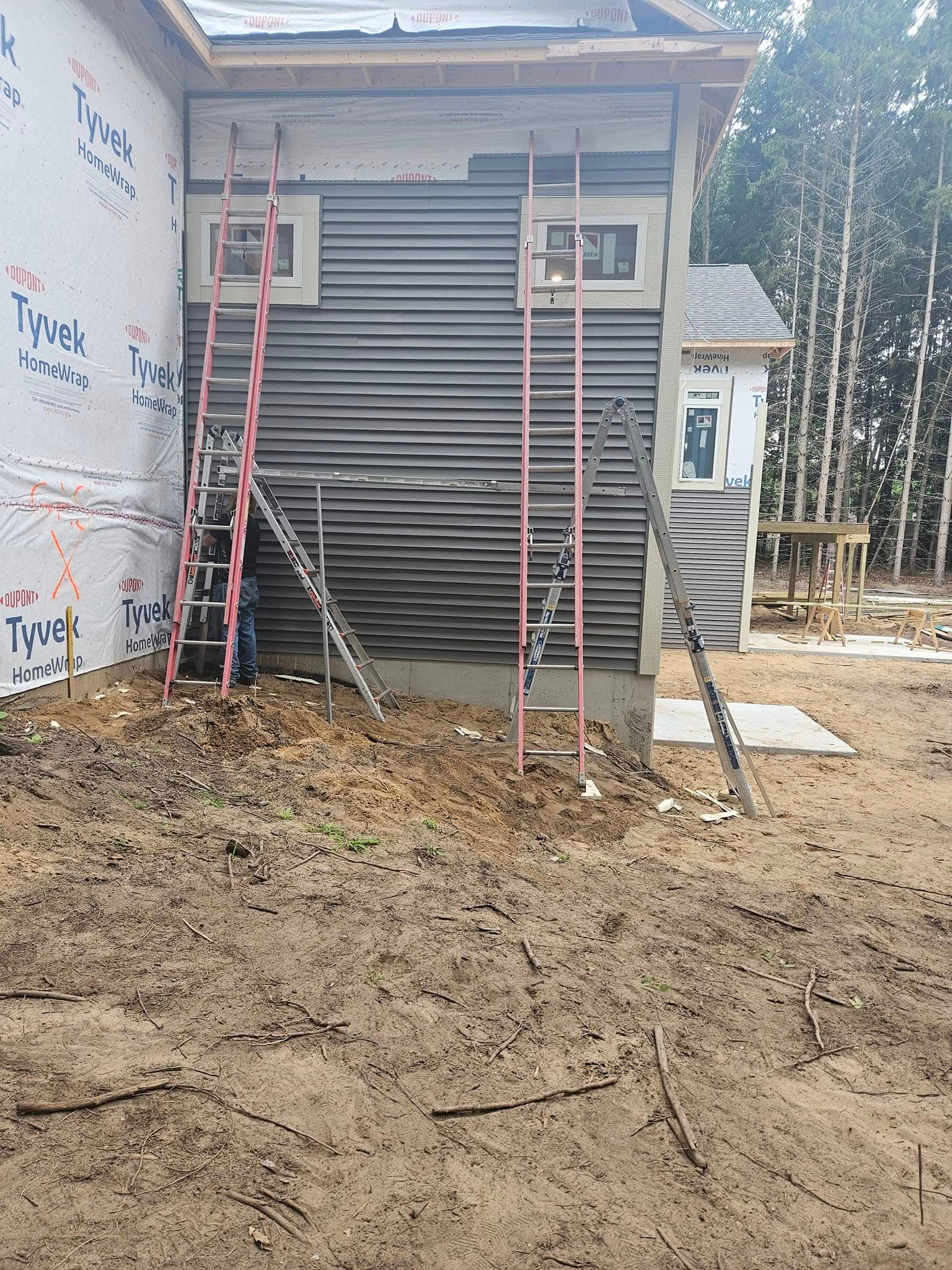 Small house under construction with two ladders and muddy ground in front