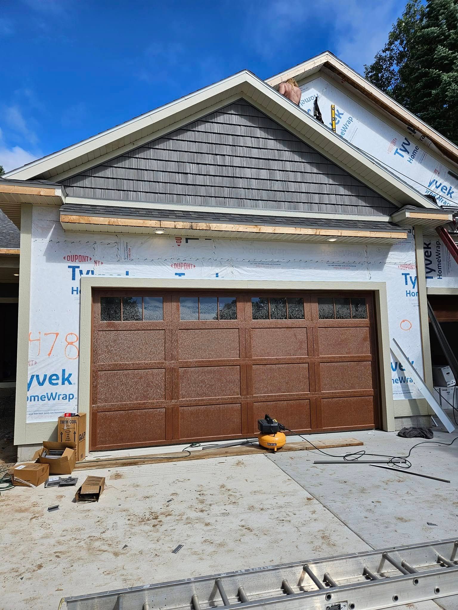 Partially built house with brown garage door, exposed siding, and construction materials on the driveway.