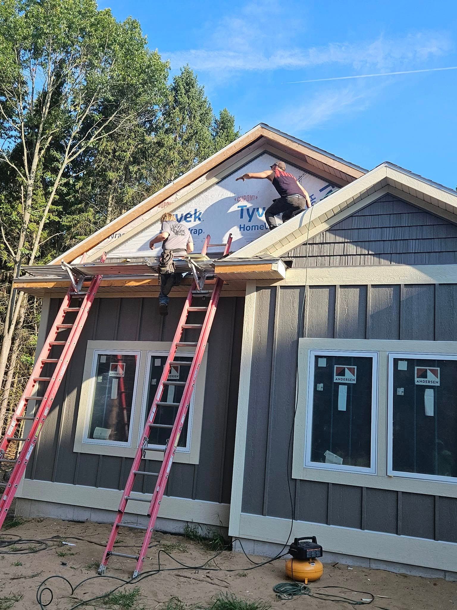 Workers on ladders installing siding and roof trim on a house under construction.