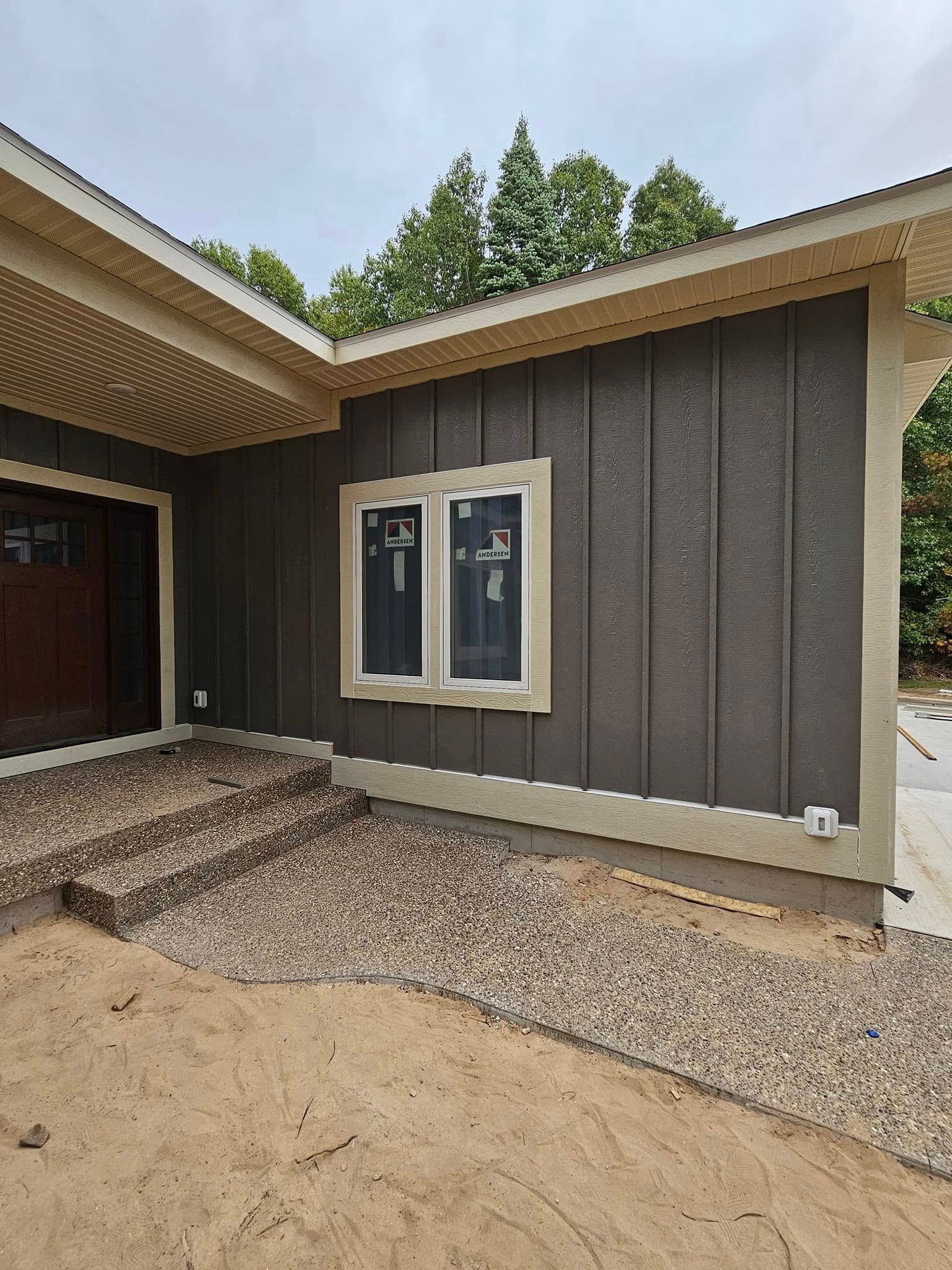 Front view of a house entrance with steps, gravel yard, and a brown exterior wall with a window.