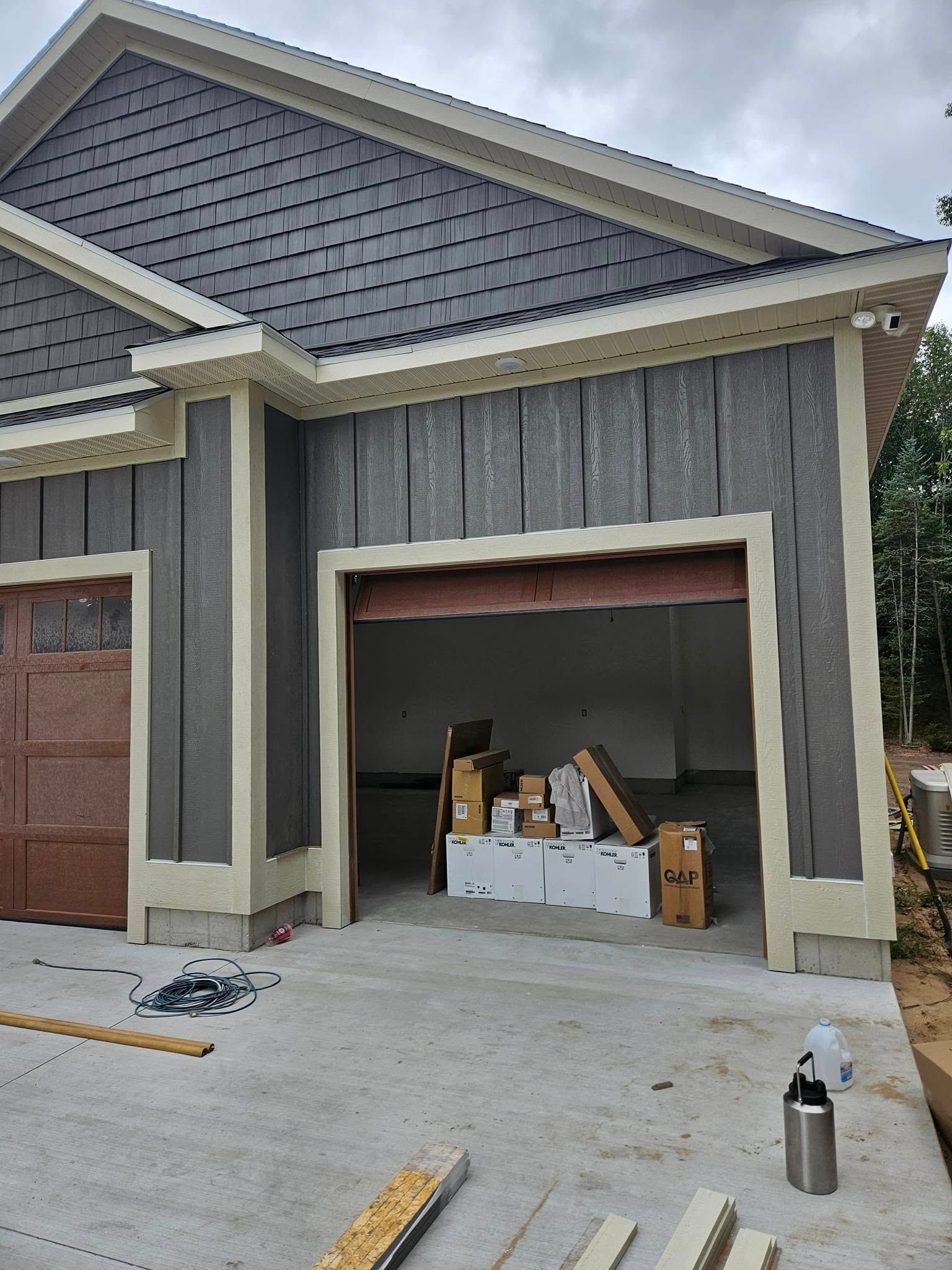 Partially finished garage with open door, construction materials inside, and tools on the driveway.