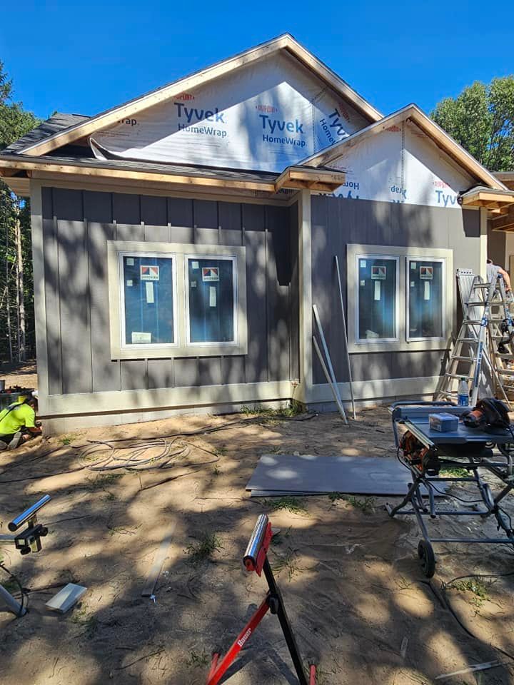 Partially built house exterior with gray siding, white trim, and construction tools in front