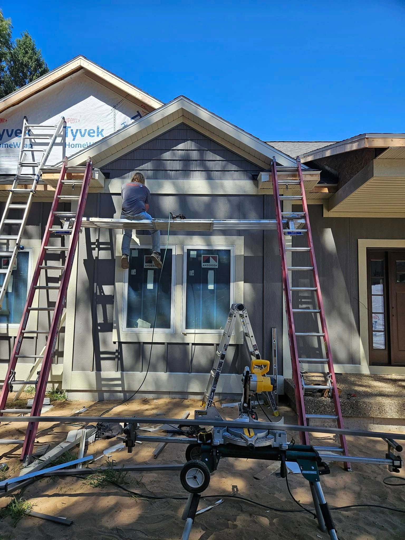 Workers on ladders installing siding on a house exterior under construction.