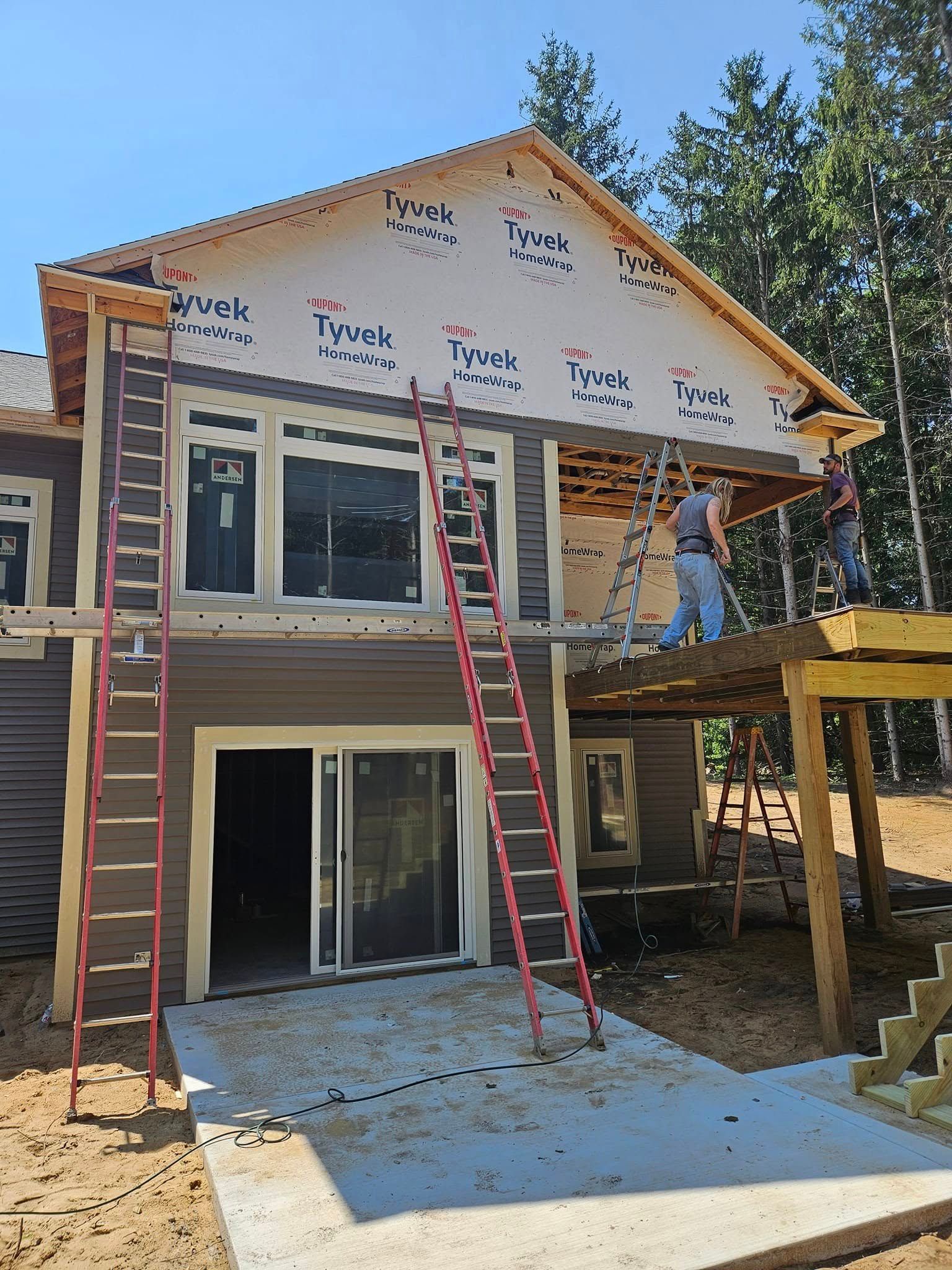 House under construction with two ladders, worker on the right, and new siding on the upper floor