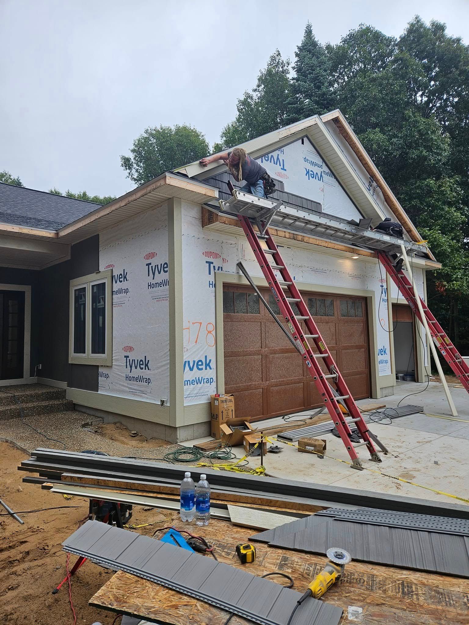 Construction workers on a roof installing siding and trim on a house with ladders and materials below
